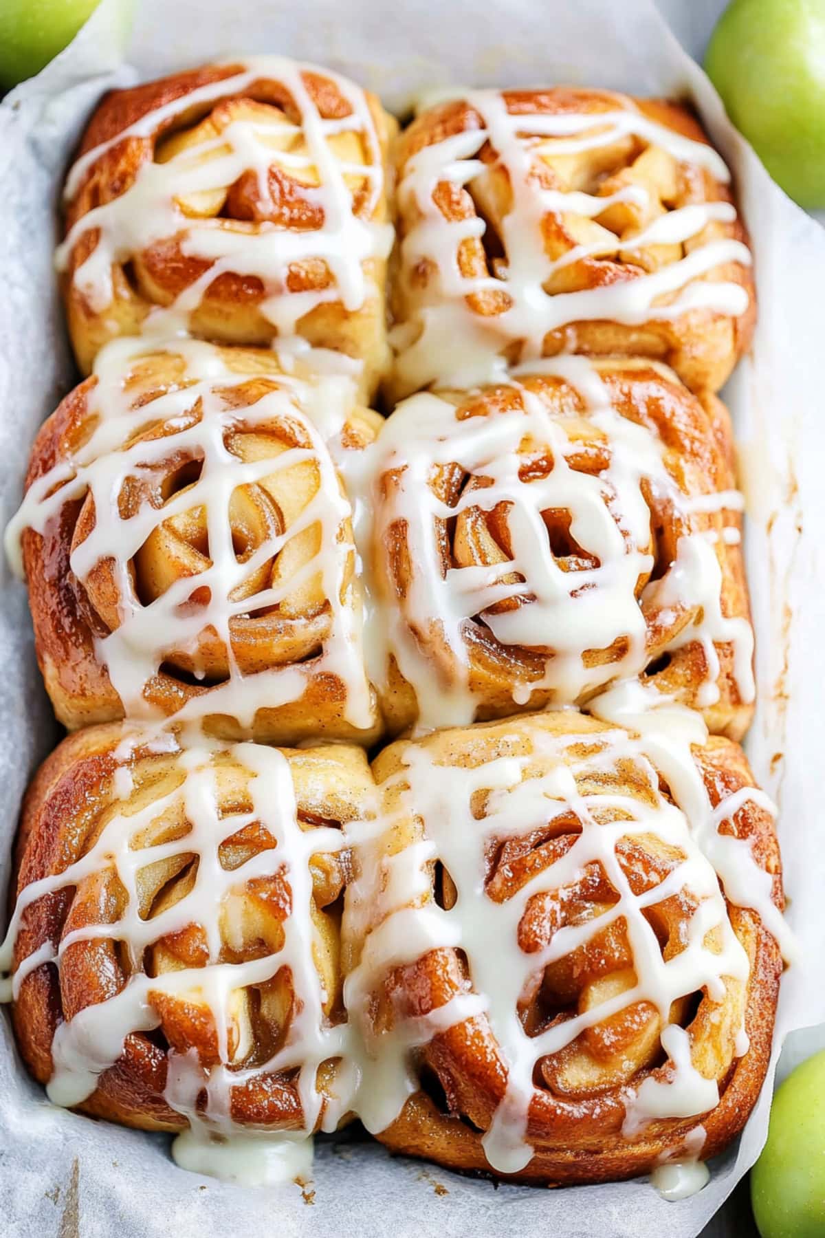 Homemade apple pie cinnamon rolls with glaze sitting on parchment paper.