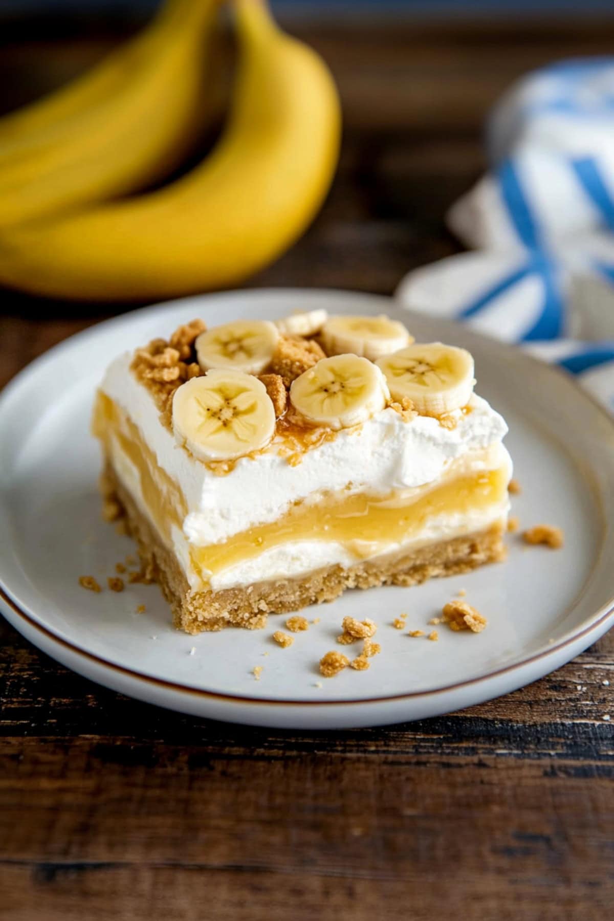 Banana cream pie bars topped with crushed nila wafers and whipped cream on a plate.