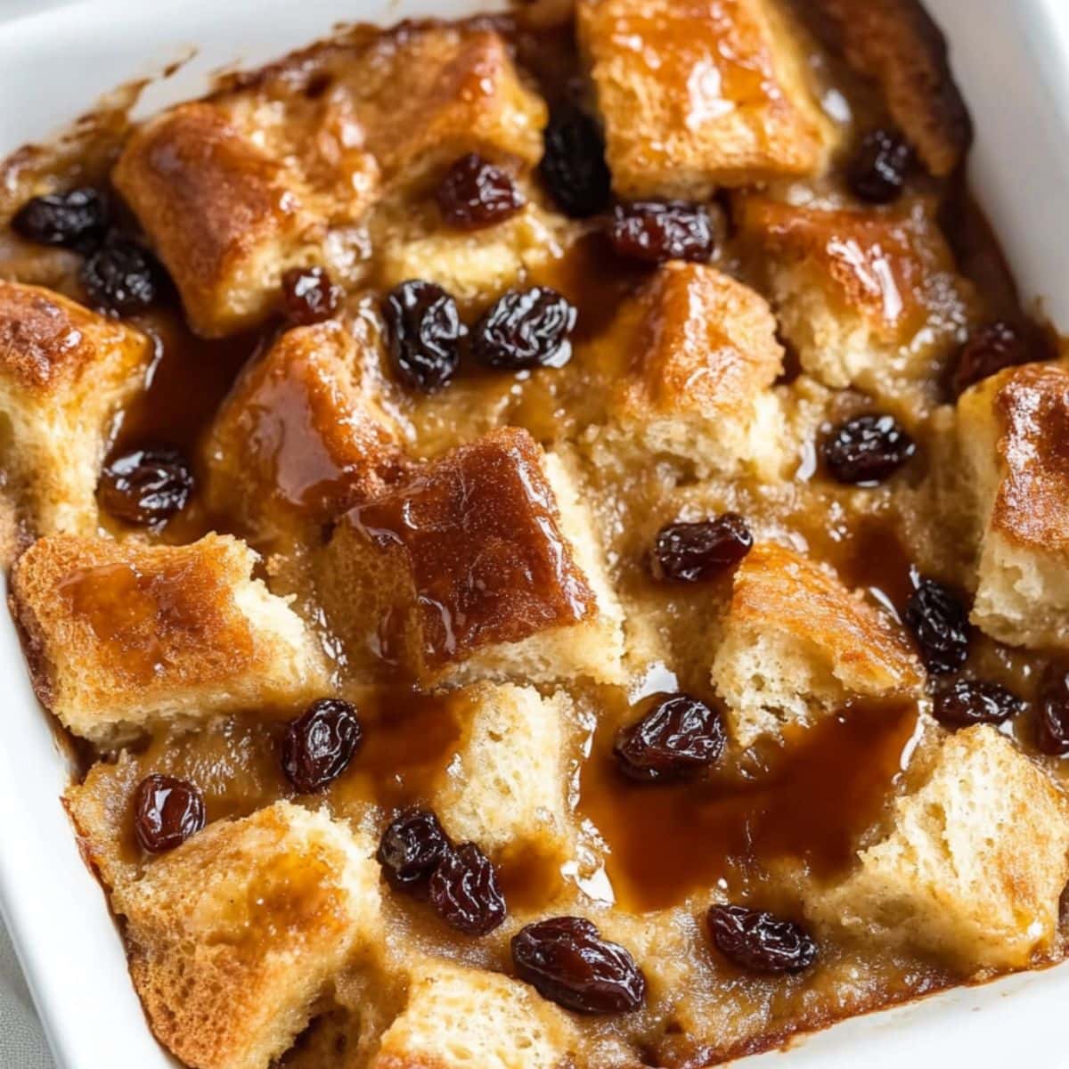 Bread pudding with syrup on top and scattered raisins baked in a square dish.