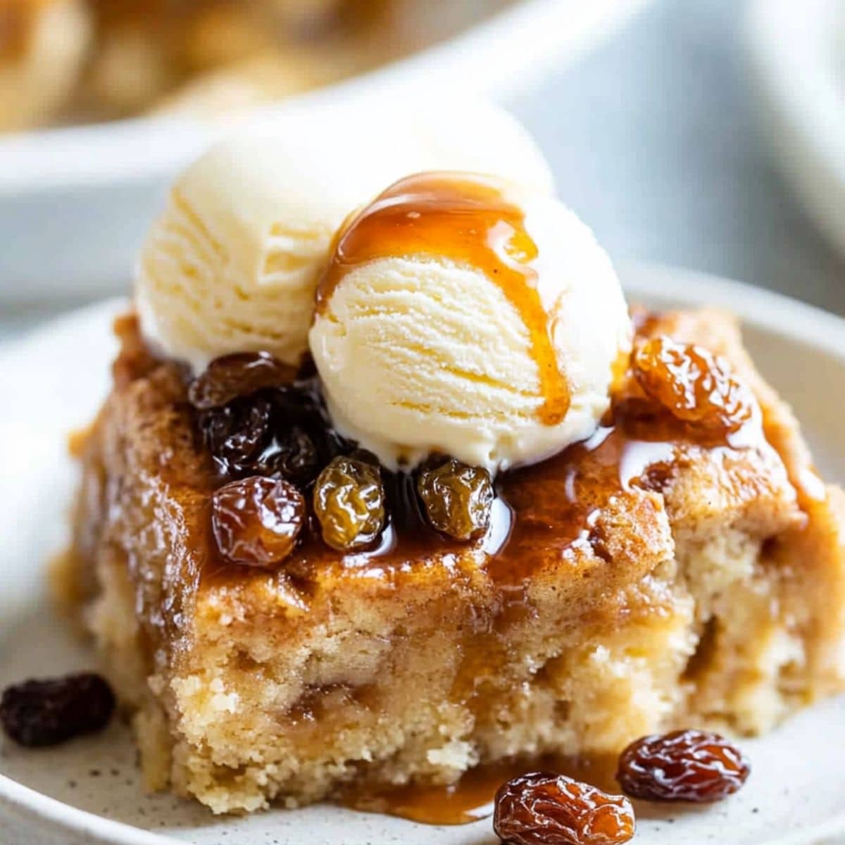 Slice of bread pudding with vanilla ice cream on top, served on a white plate.