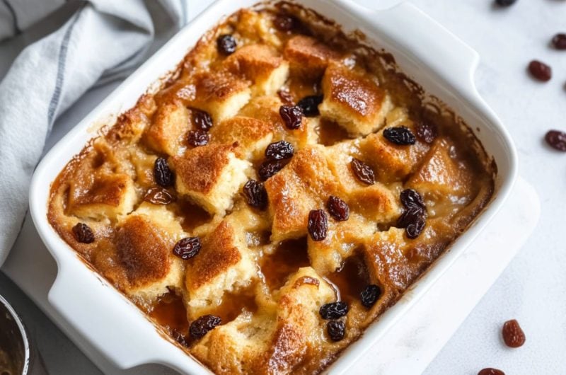 Bread pudding in a white baking dish with raisins and bourbon syrup on top.