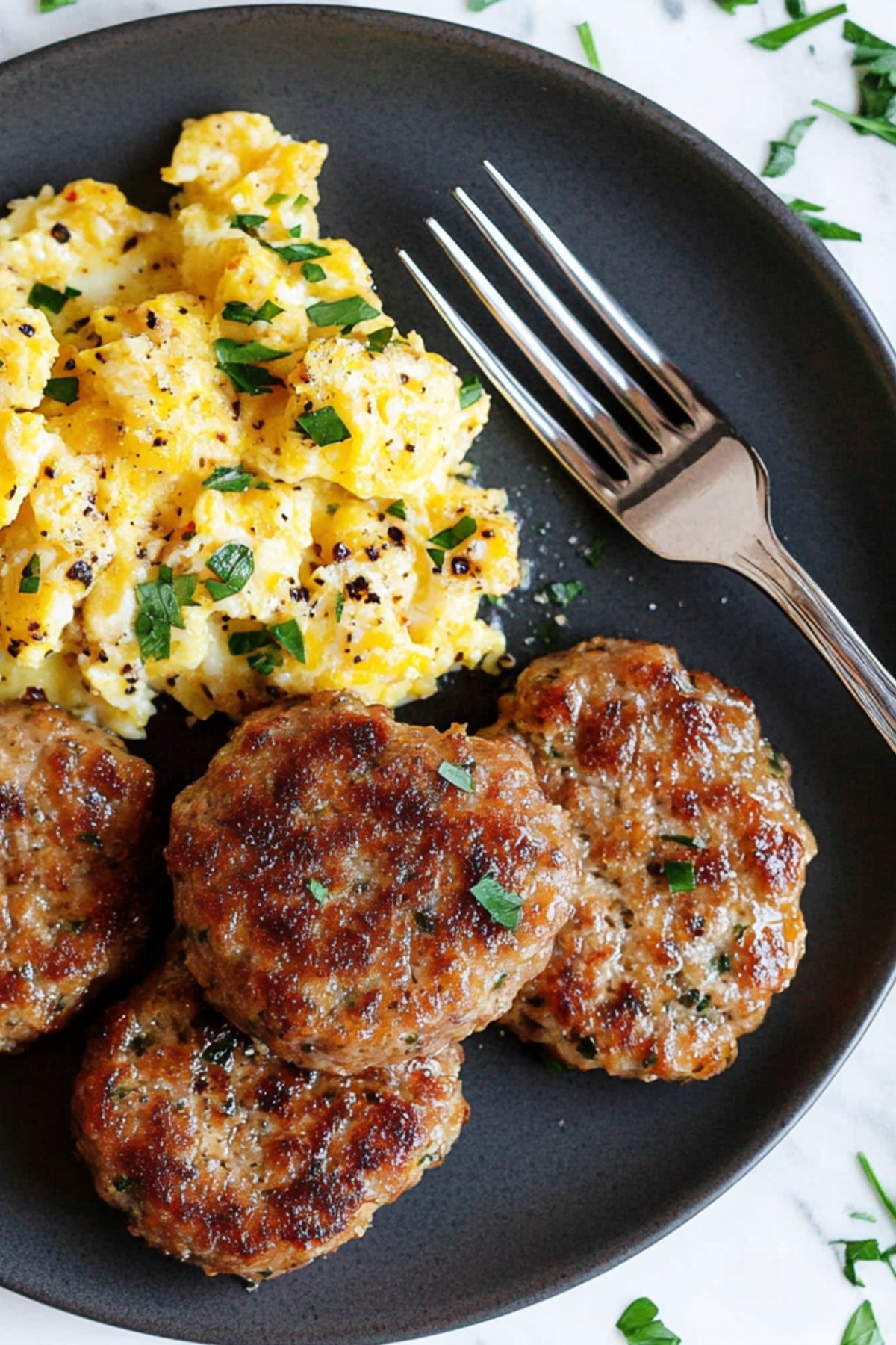 Savory breakfast sausage patties with scrambled eggs in a black plate.