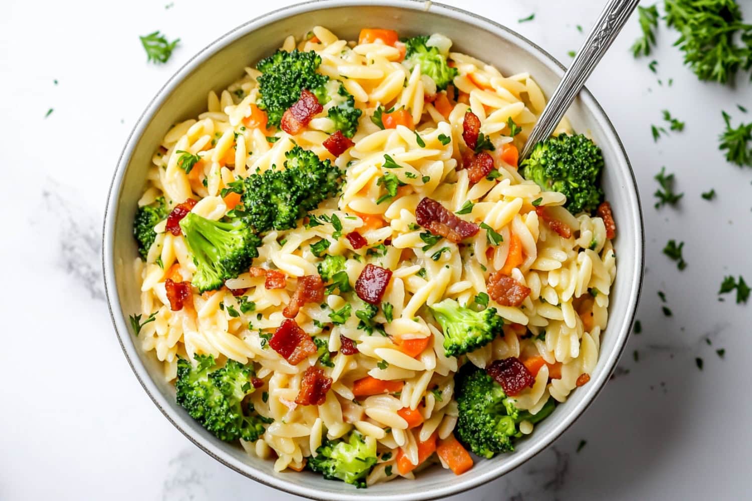 An overhead view of broccoli cheddar orze with bacon and carrots.