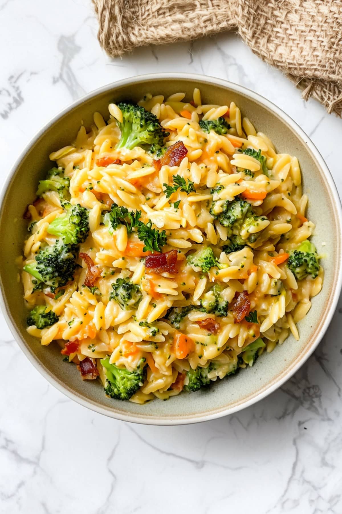 A bowl of cheesy broccoli cheddar orzo with bacon and carrots.