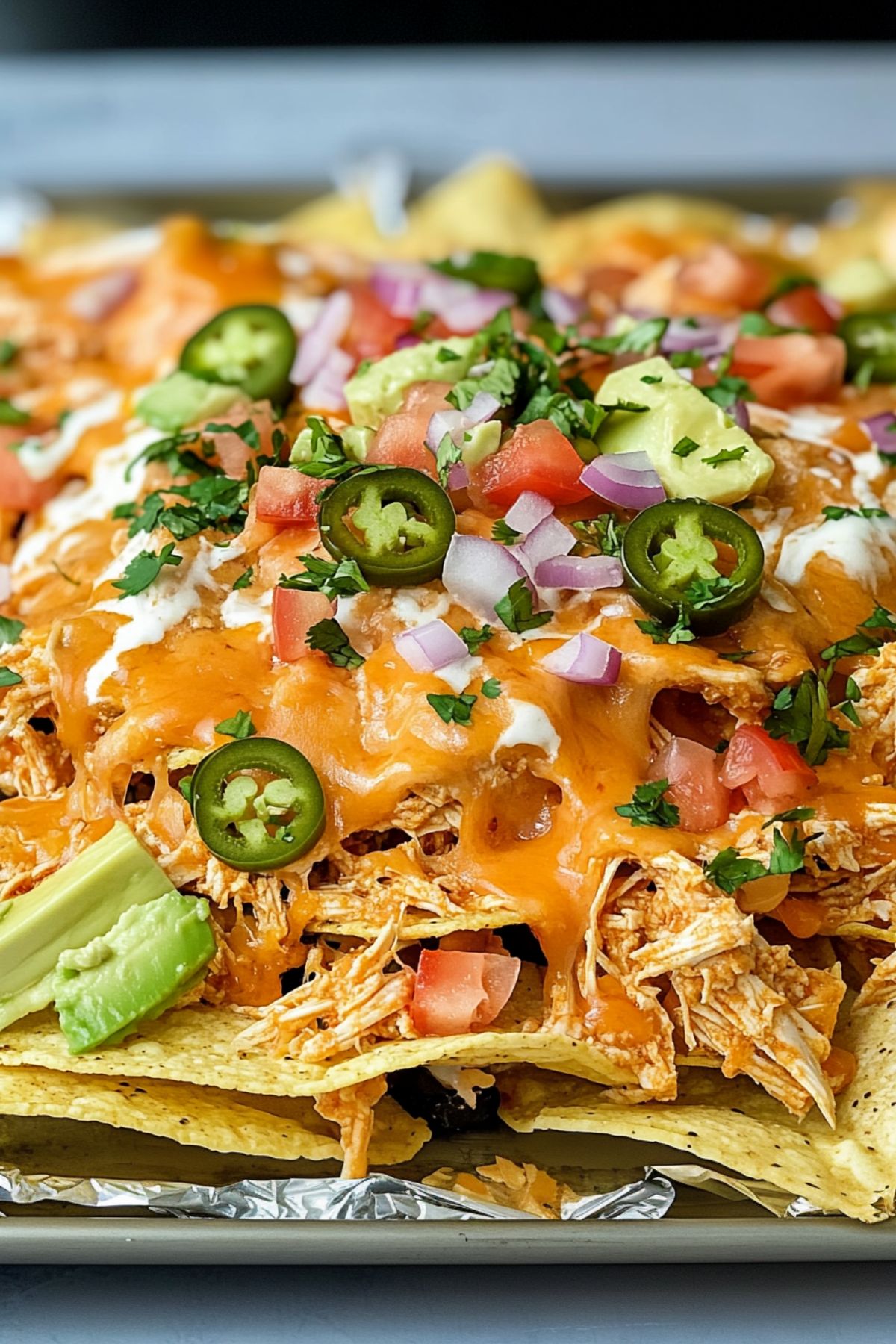 Shredded chicken with buffalo sauce served on top of nachos in a baking sheet pan with aluminum foil. 