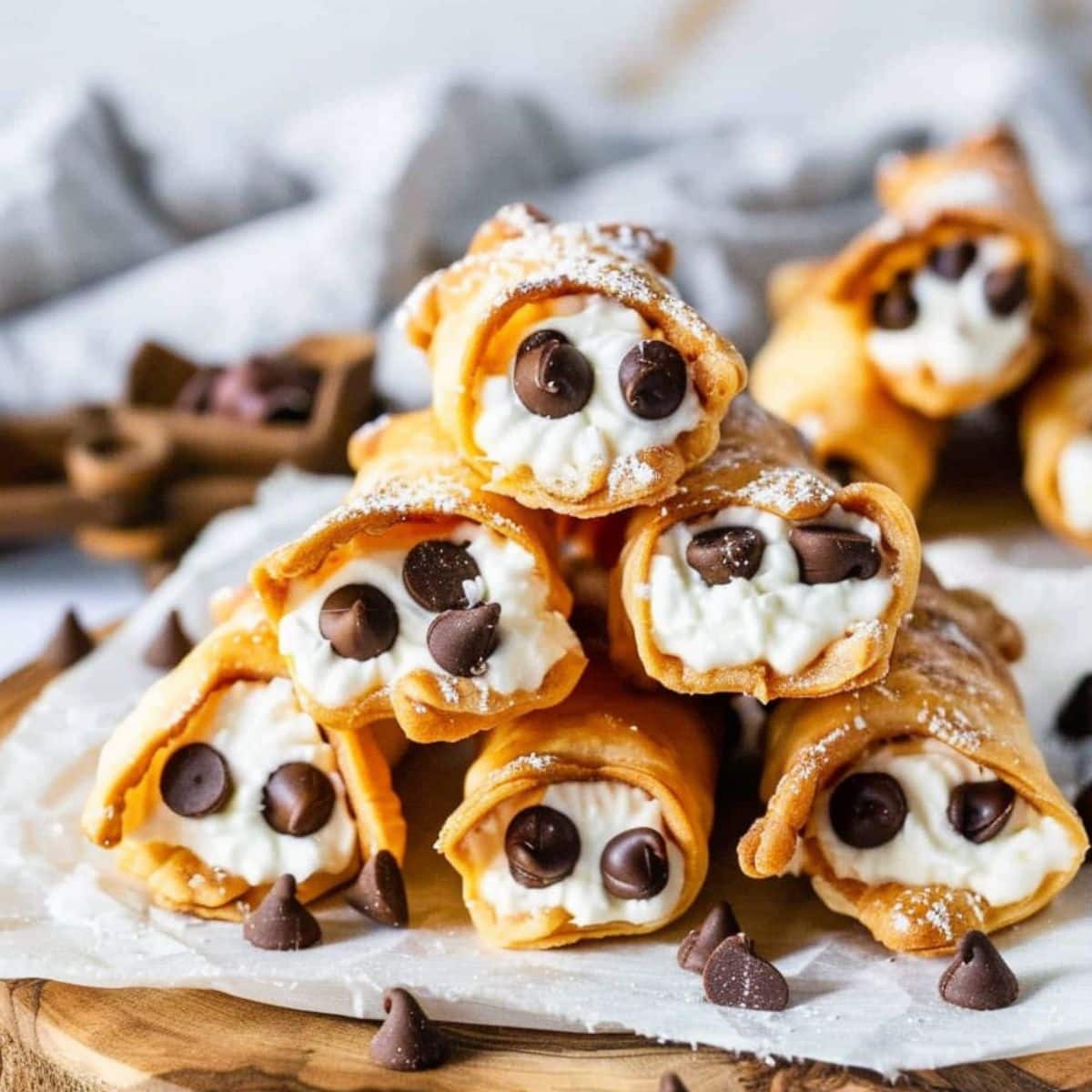 Bunch of cannoli stacked on top of each other sitting on a wooden board with parchment paper.