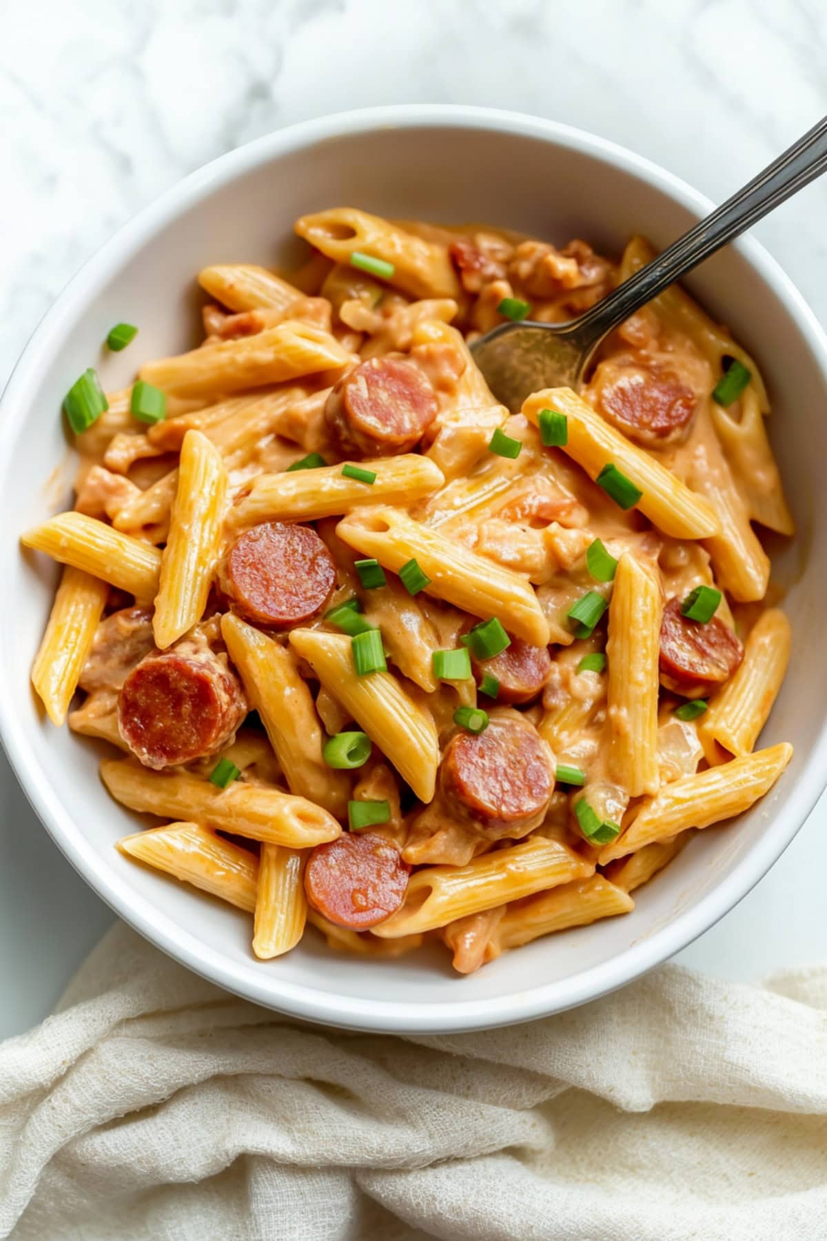 An overhead view of cheesy kielbasa pasta on a white marble table.