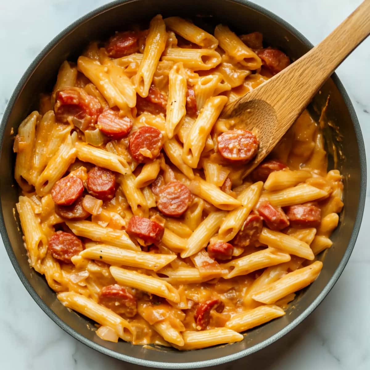 A saucepan filled with cheesy kielbasa pasta and chopped onions.