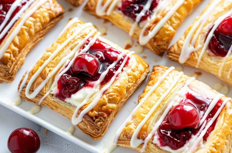 Cherry cream cheese Danish arranged in a white tray drizzled with sugar glaze on top.