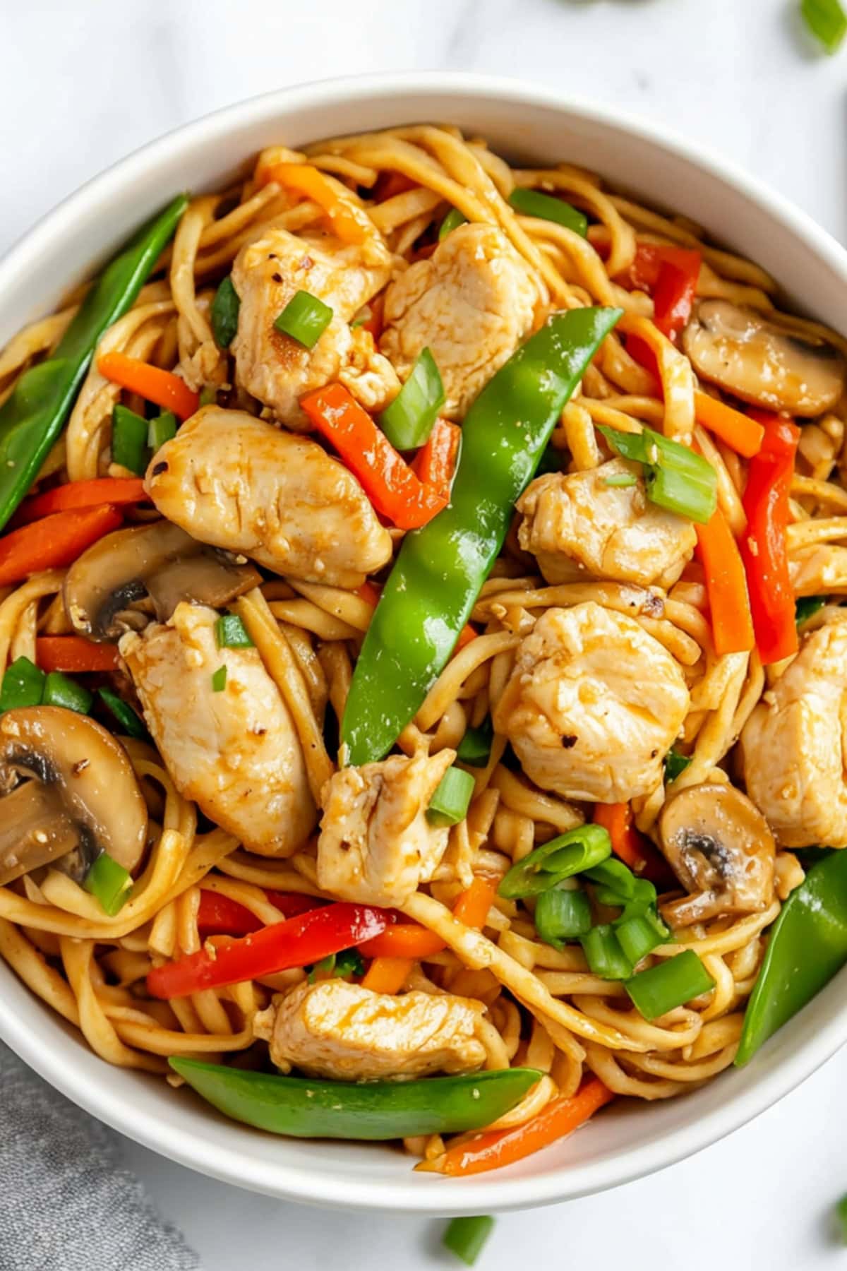 A plate of chicken lo mein noodles stir-fried with colorful vegetables, including bell peppers, carrots and snow peas.