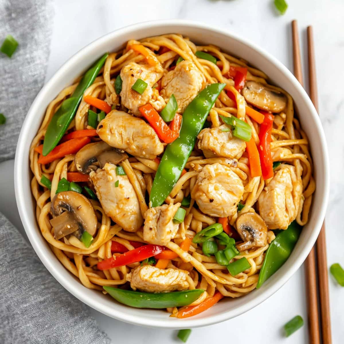 A bowl of chicken lo mein with mushrooms, carrots, bell peppers and green onions.