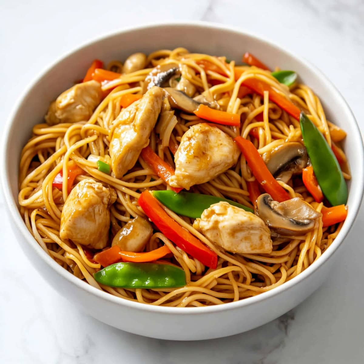 A steaming bowl of chicken lo mein featuring stir-fried vegetables tossed with soft, golden noodles.