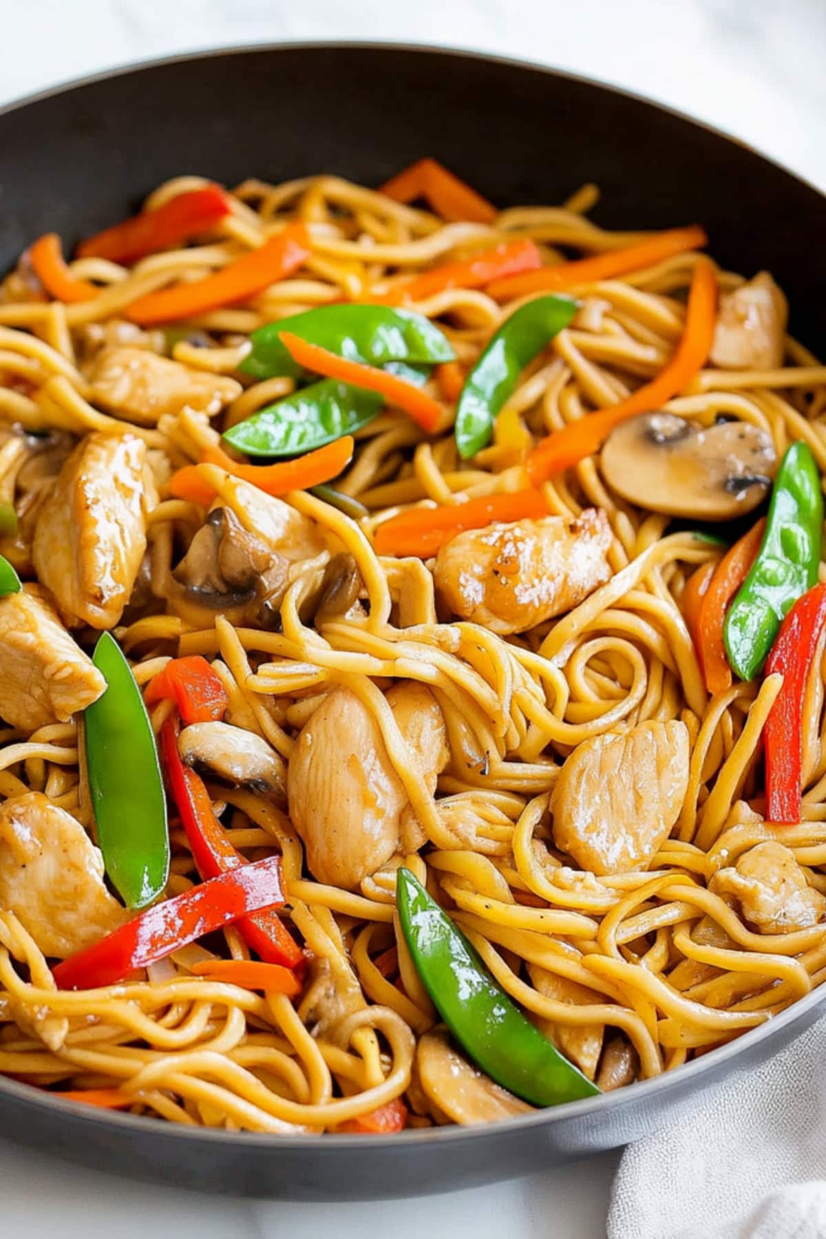 Chicken lo mein with snow peas,bell peppers and carrots in a skillet.