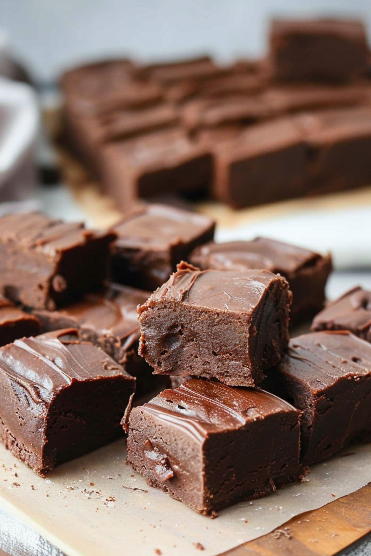 Square pieces of creamy chocolate fudge on parchment paper on a wooden board.