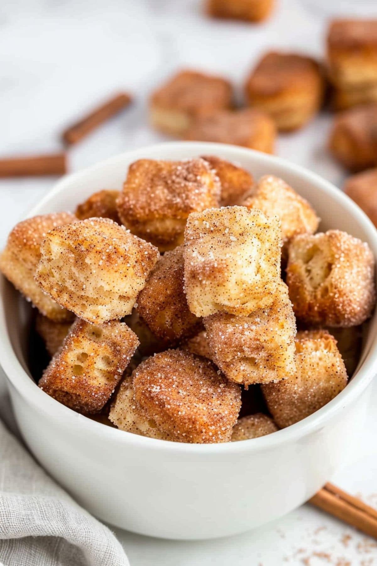 Bunch of cinnamon sugar coated biscuits bites in a white bowl.