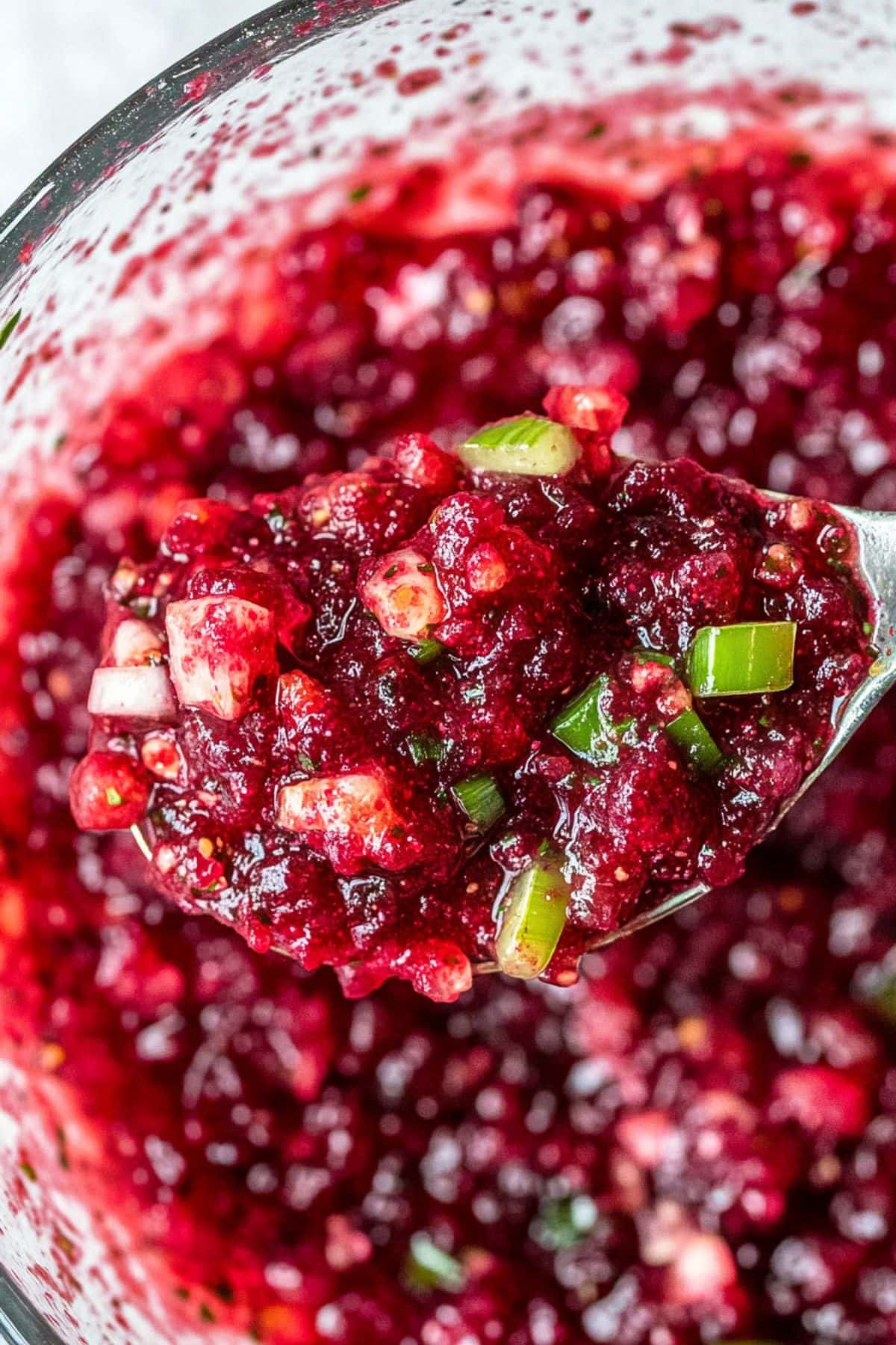 Spoon lifting a serving of cranberry salsa from a mixing bowl, close up.