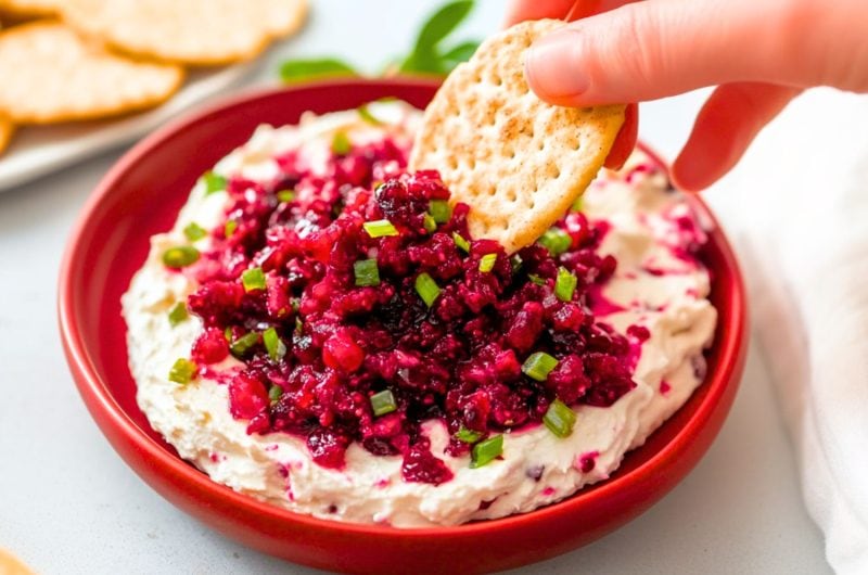 Cracker dipped over cranberry cream cheese dip served in a red plate.