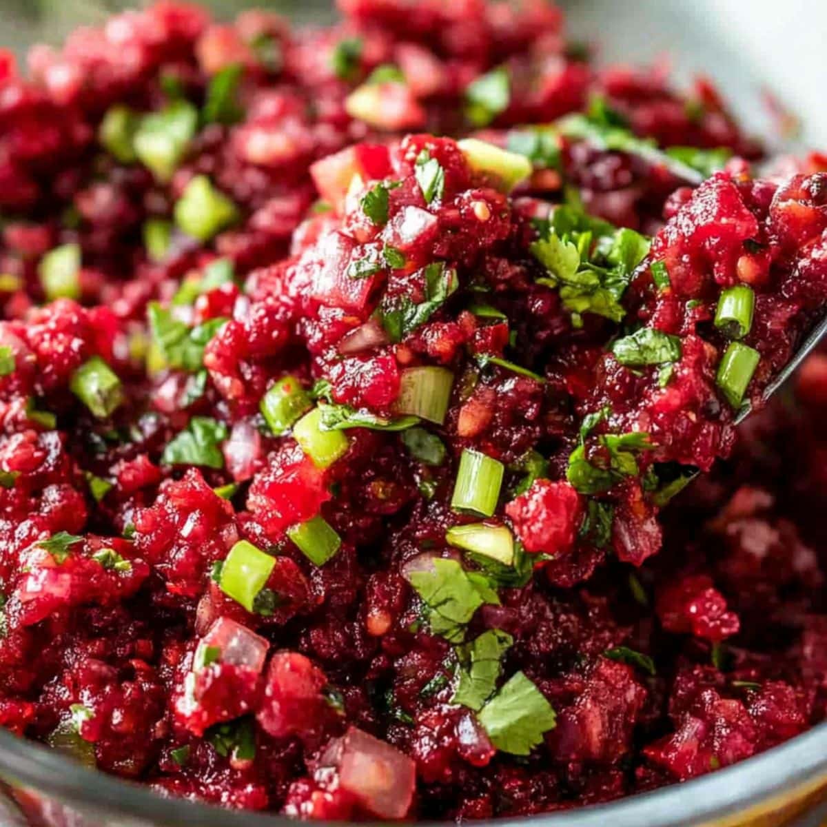 Finely chopped cranberries with cilantro, green onions and jalapenos in a glass bowl.