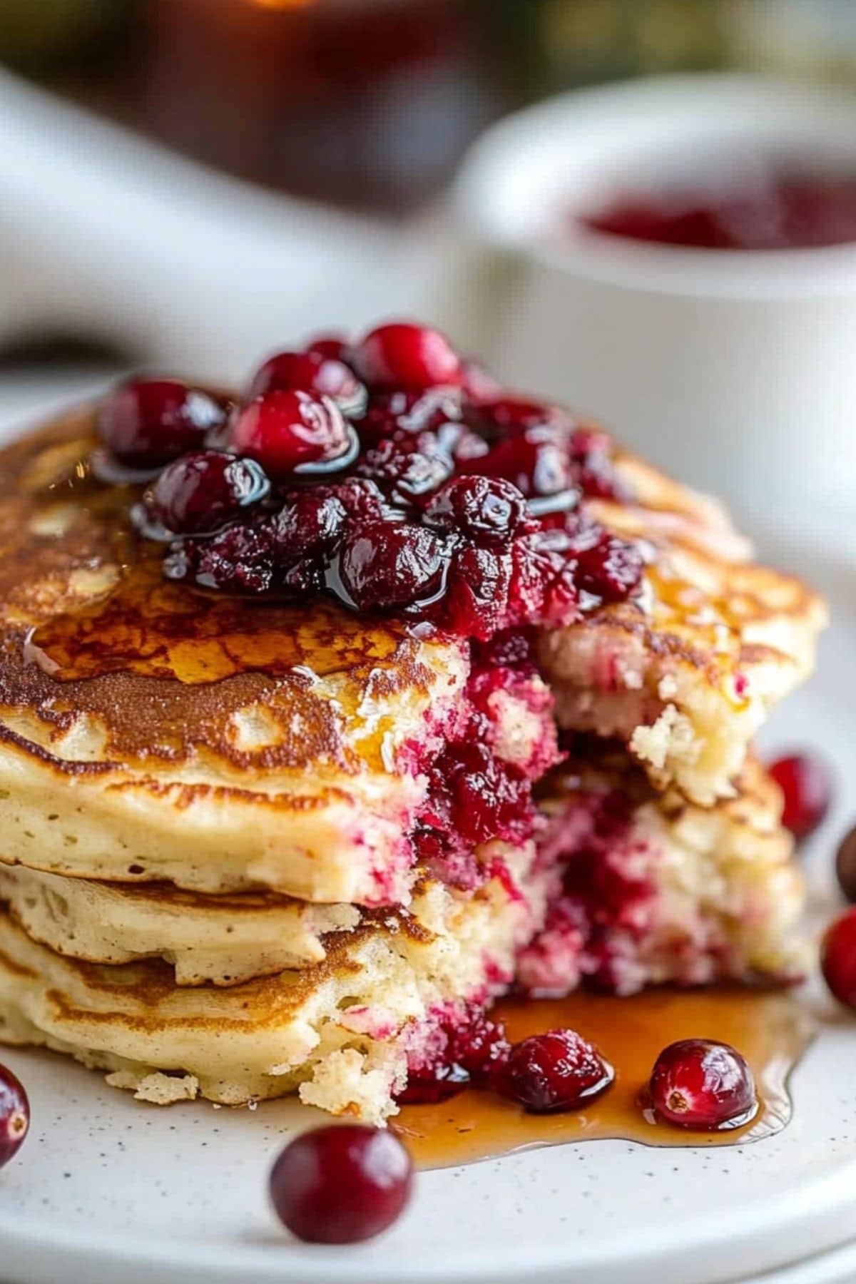 Cranberry pancakes, portion sliced served with cranberries and syrup in a white plate.