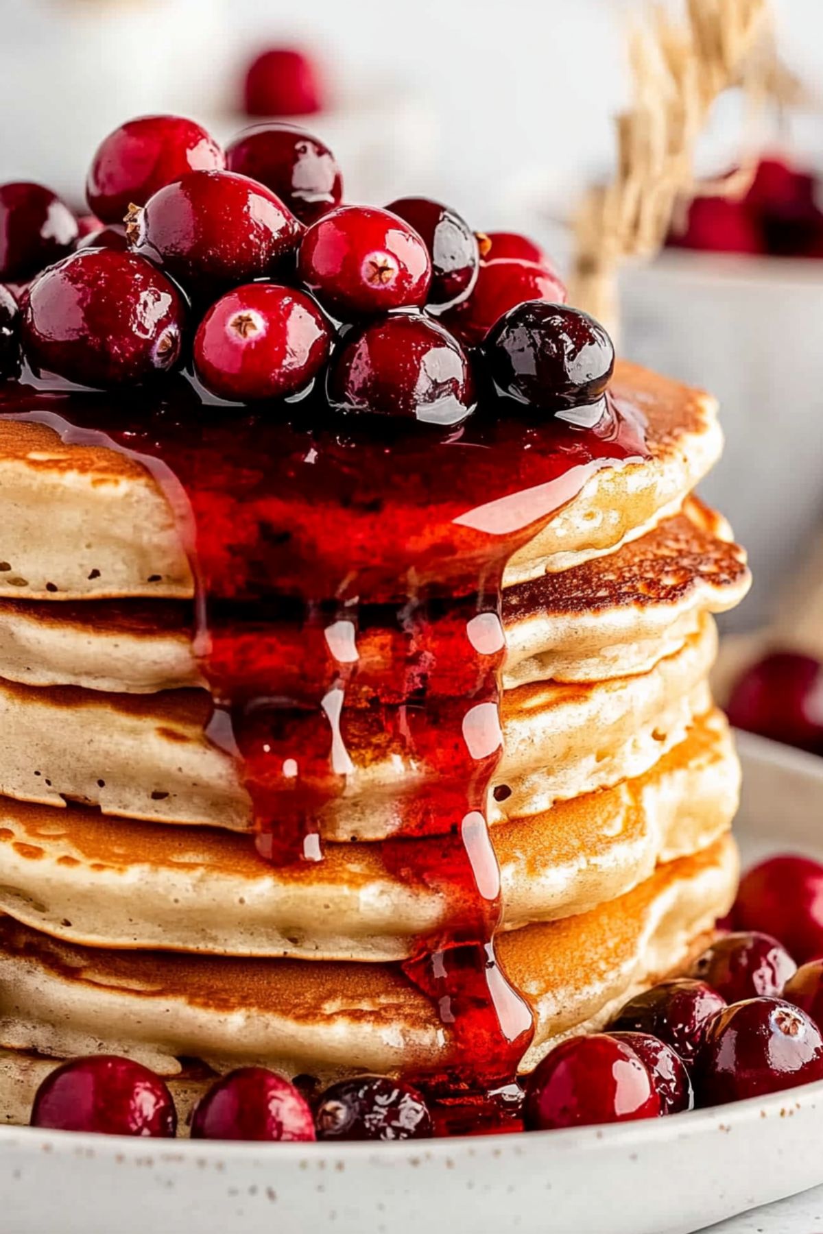 Stacked fluffy and thick pancakes garnished with fresh cranberries and syrup.