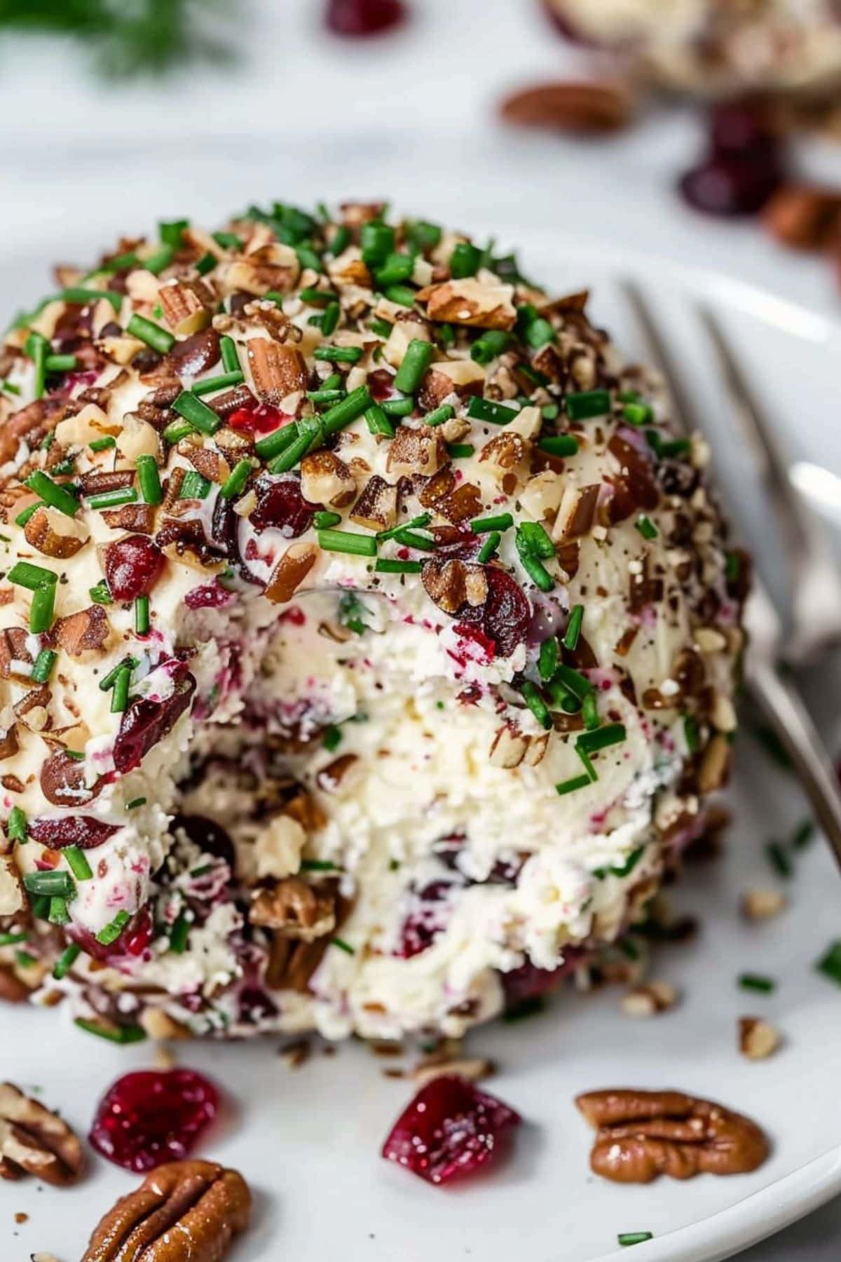 A pecan cranberry cheese ball served on a white plate with a portion missing