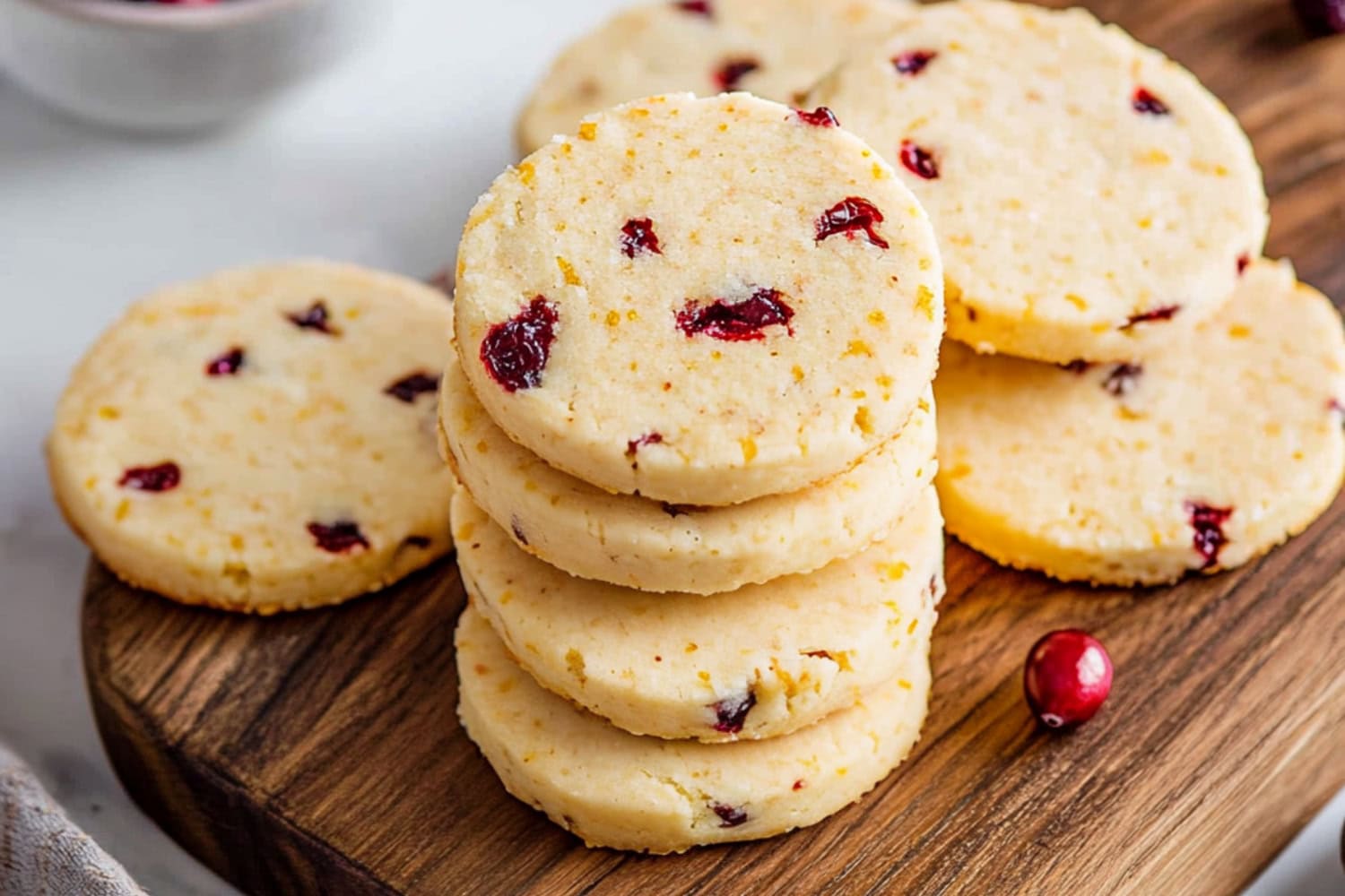 A close-up view of cranberry orange shortbread cookies with a crumbly texture in a wooden board.