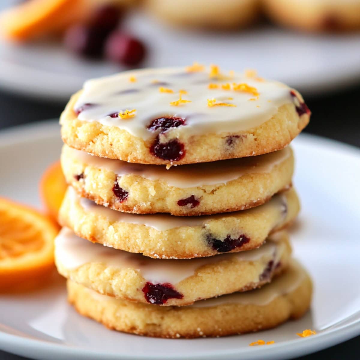 Close-up of cranberry orange cookies with glaze and orange zest in a white plate.