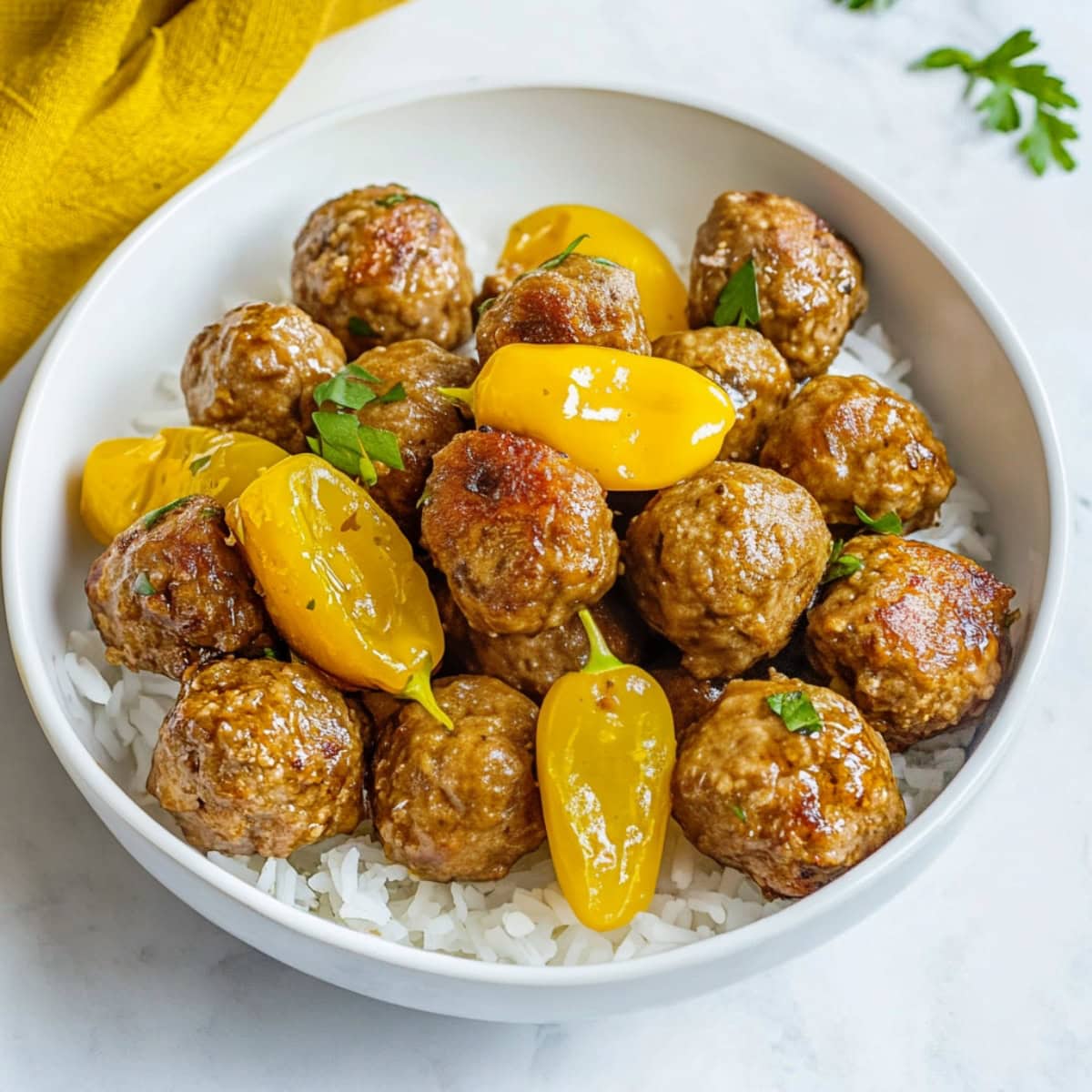 A close-up of Mississippi meatballs served over rice with pepperoncini peppers.