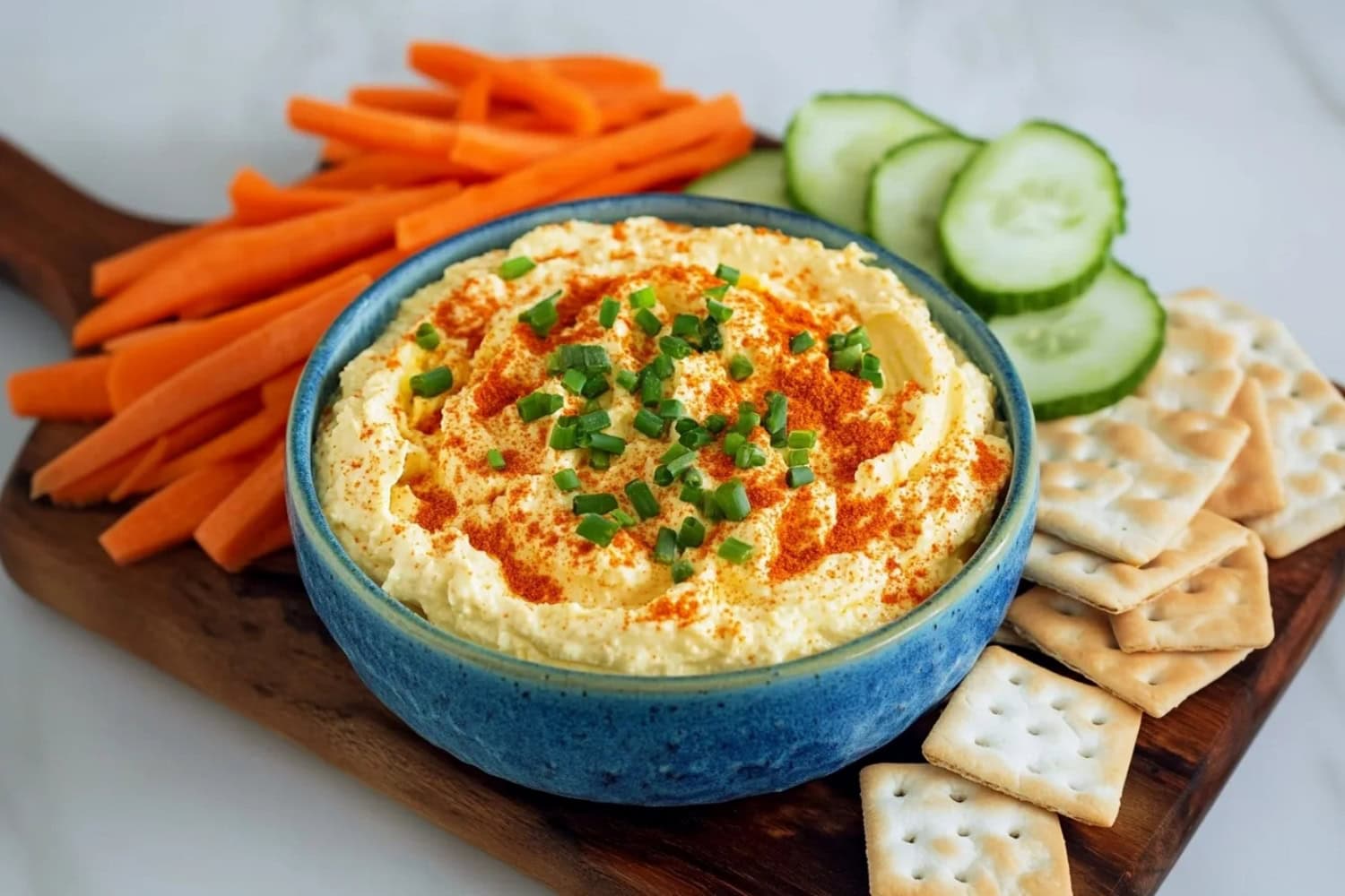 A bowl of creamy homemade deviled egg dip with fruits and crackers in a wooden board.