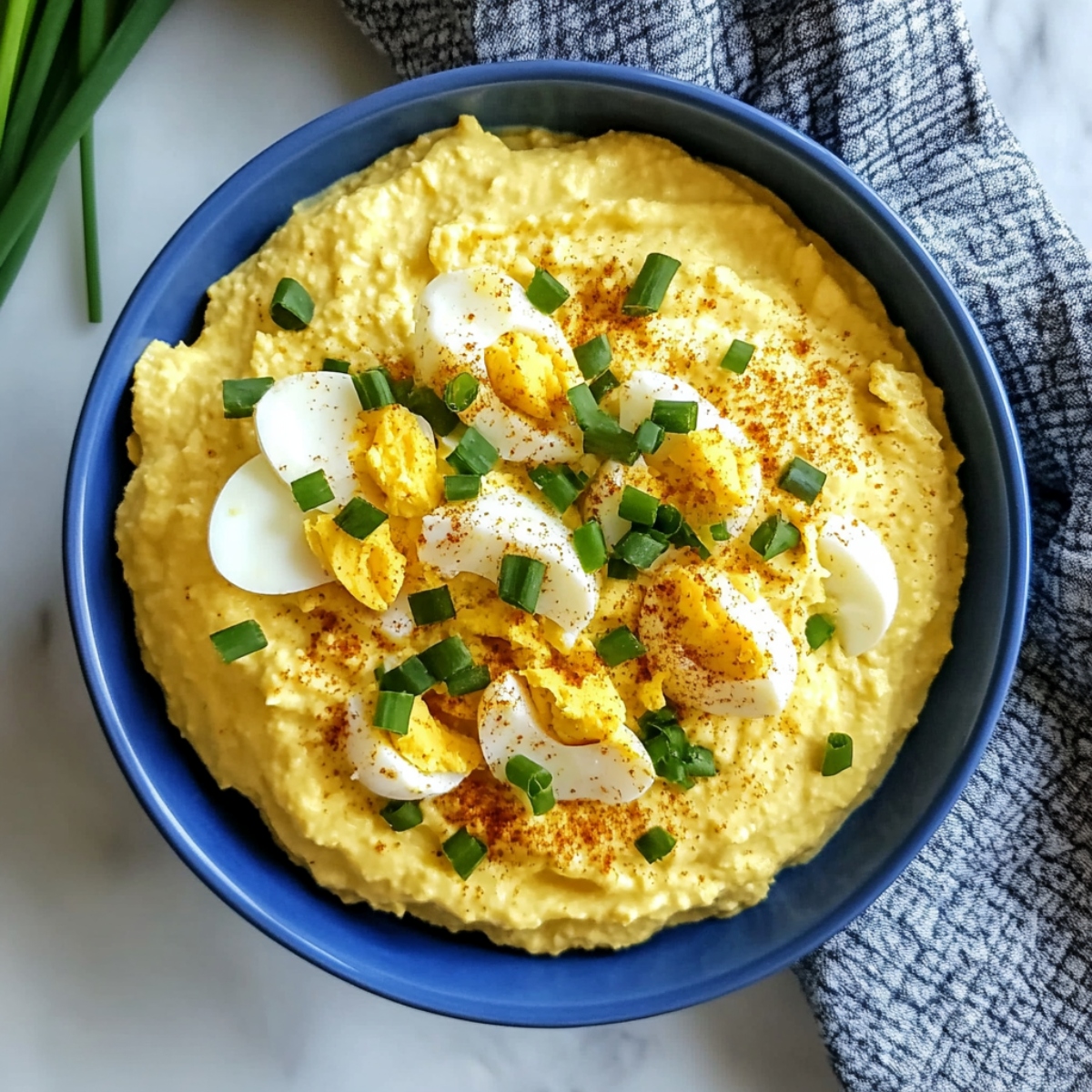 An overhead view of deviled egg dip with chopped chives and paprika.