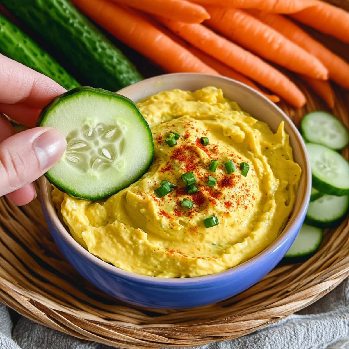 A hand dipping a cucumber into a bowl of deviled egg dip.