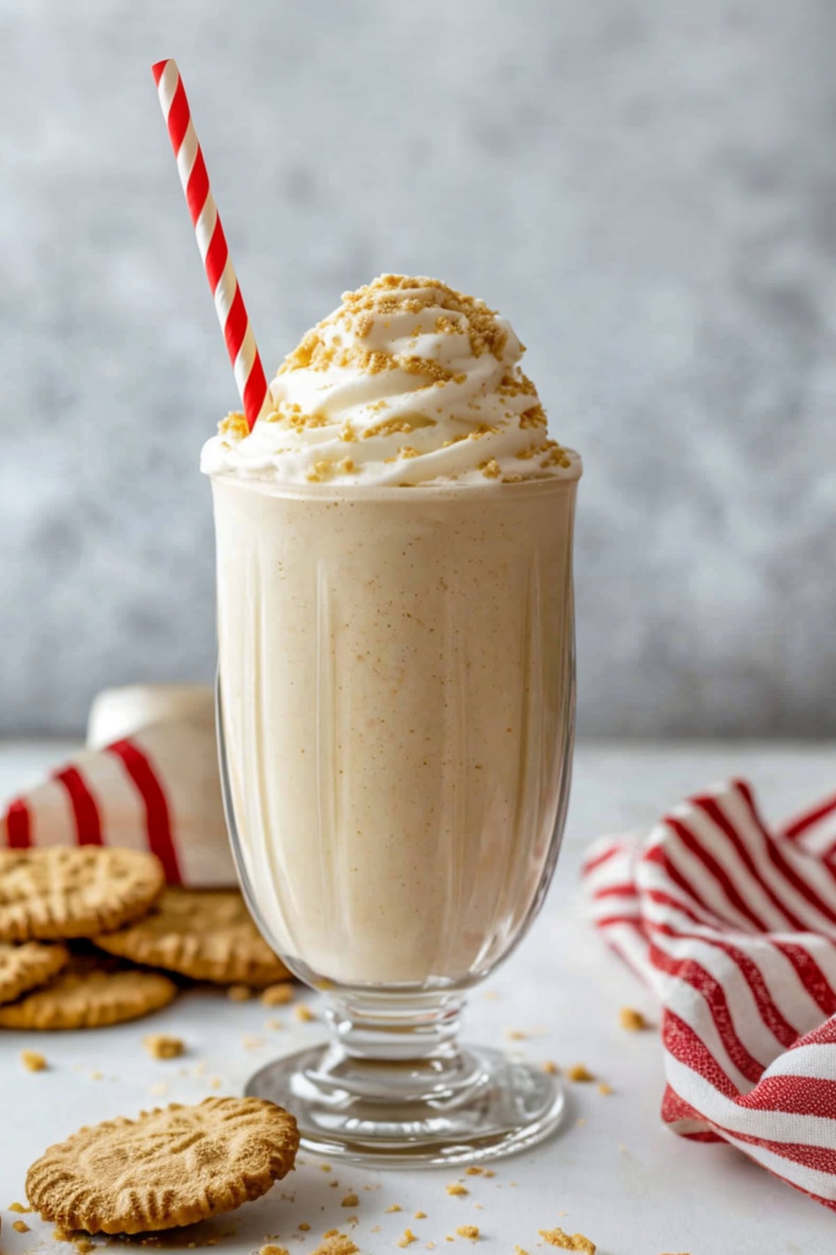 A tall glass of eggnog milkshake with whipped cream and crushed cookies on top.