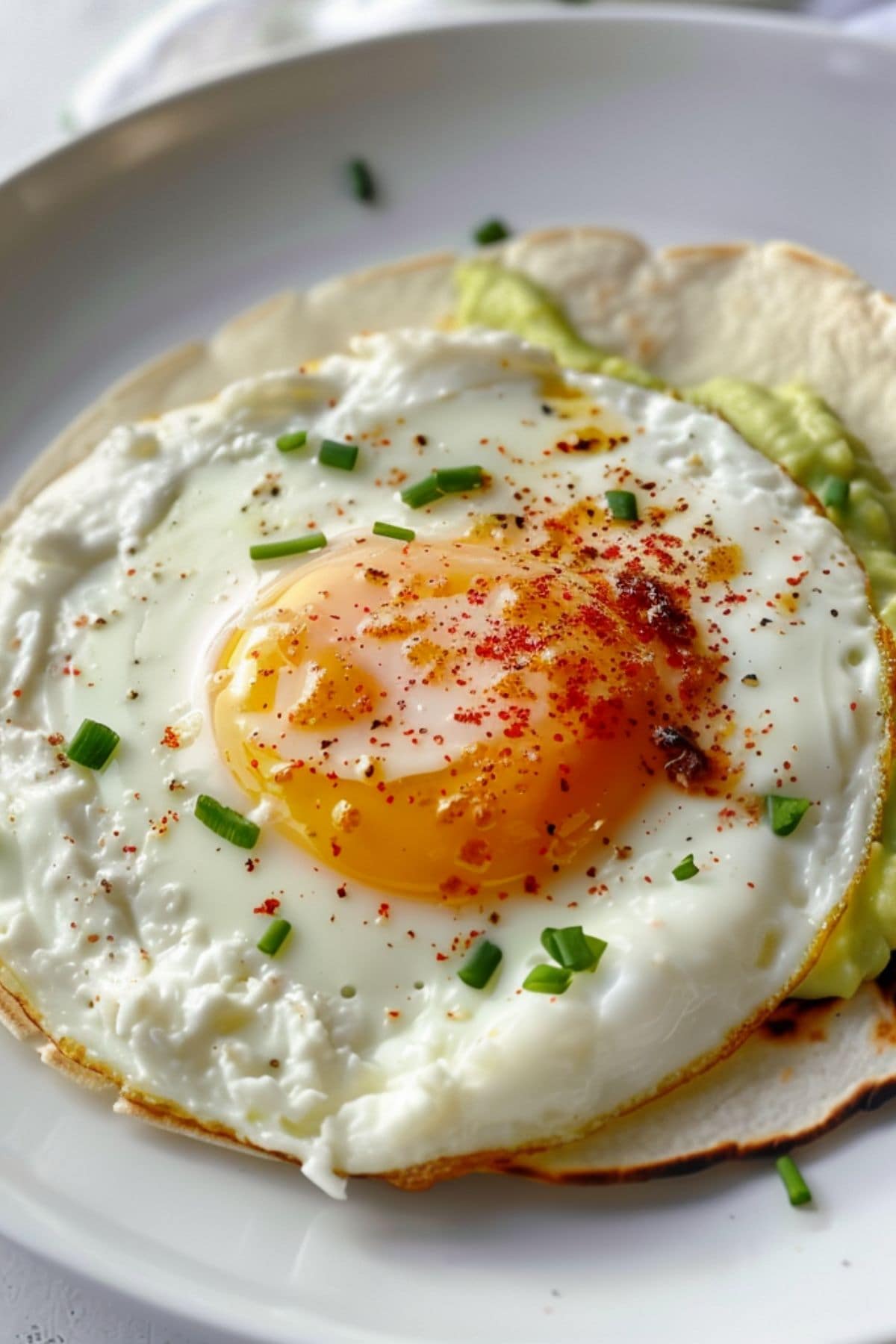 Fried sunny side egg with melted crumbled feta cheese on eges served on top of tortilla with mashed avocado spread.