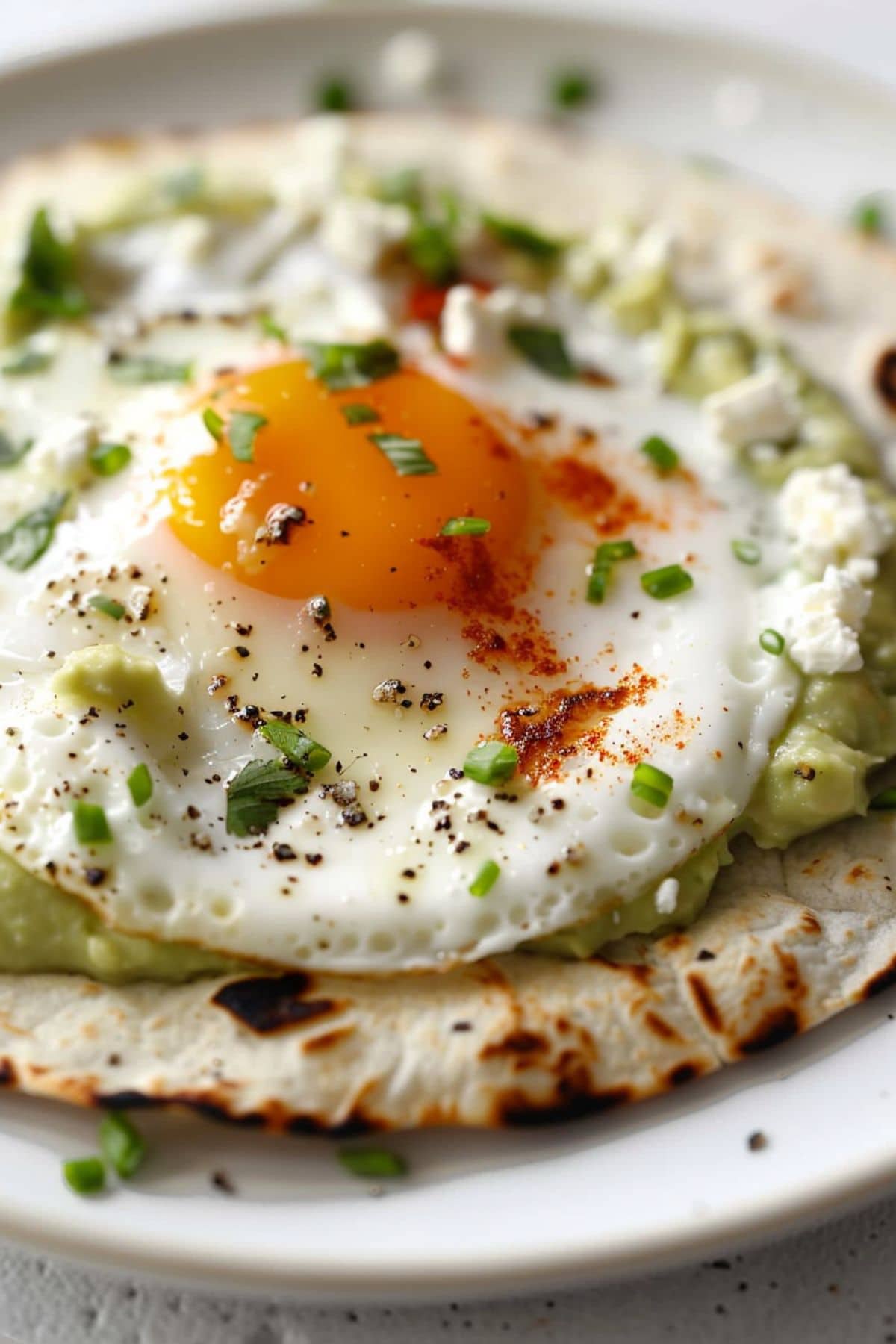 Fried eggs with melted feta cheese on edges served on top of tortilla with avocado spread.