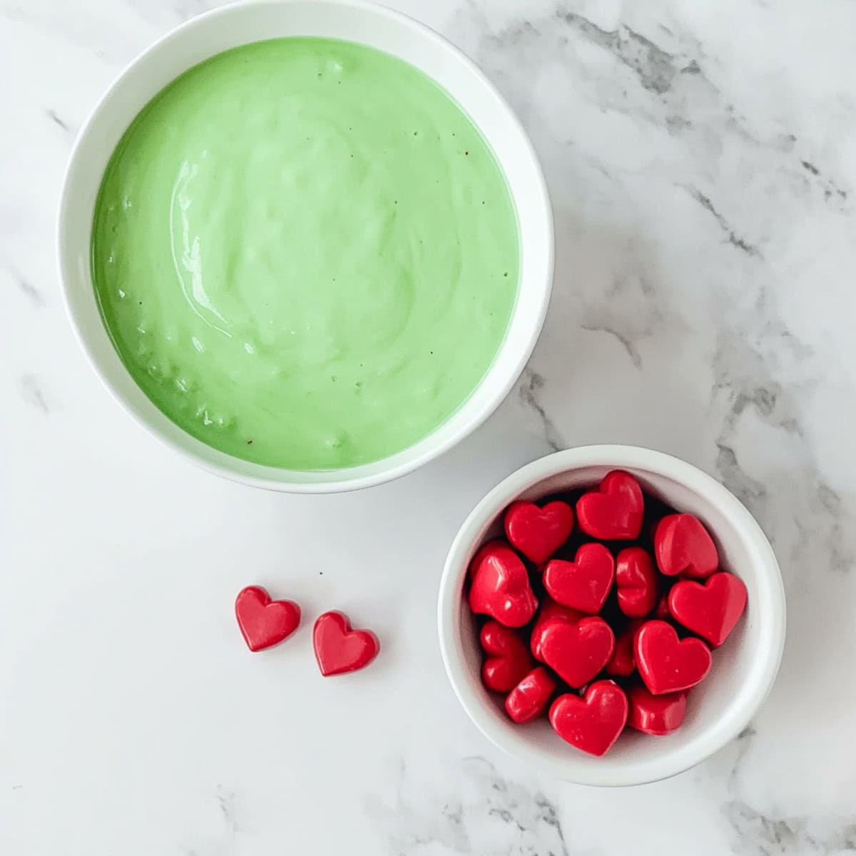 Bowls colored green cream and heart candies on a marble table.