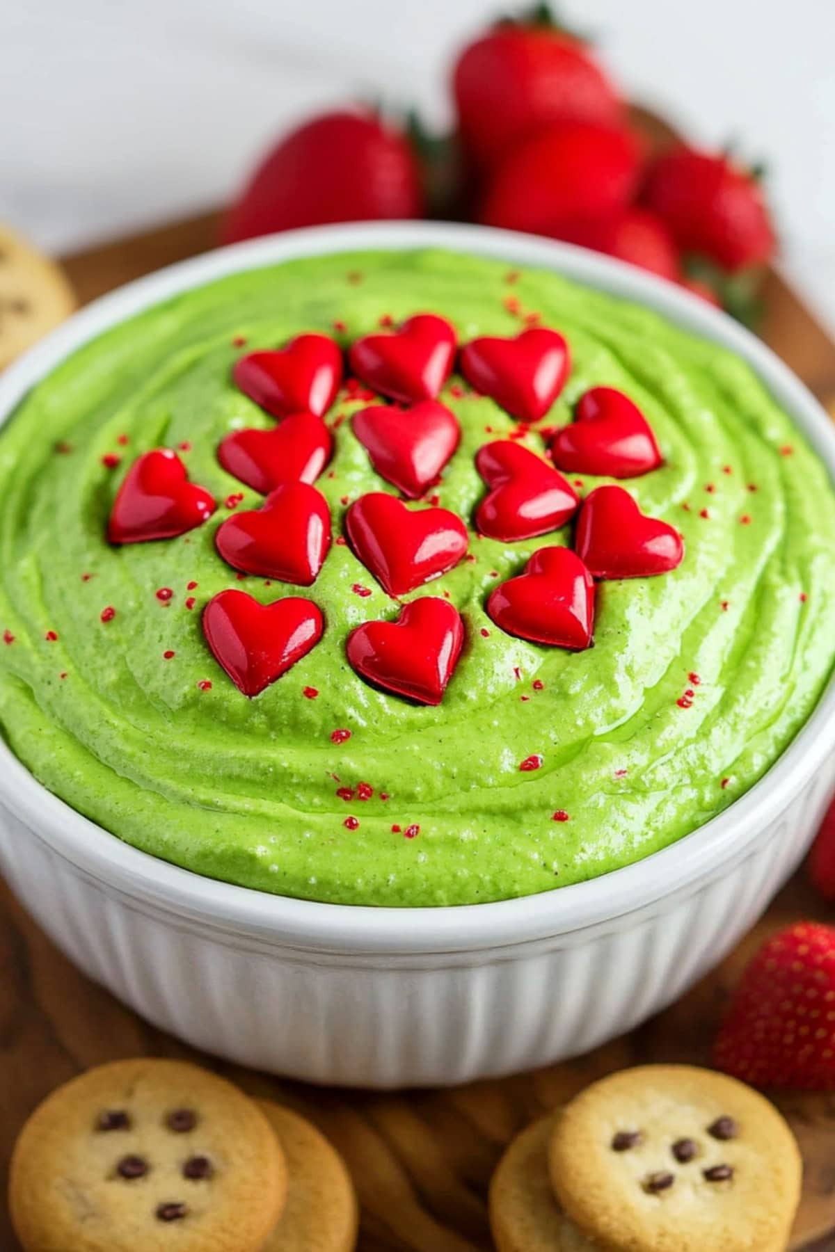 Festive grinch dip in a bowl on a wooden board with fresh red strawberries and savory cookies.