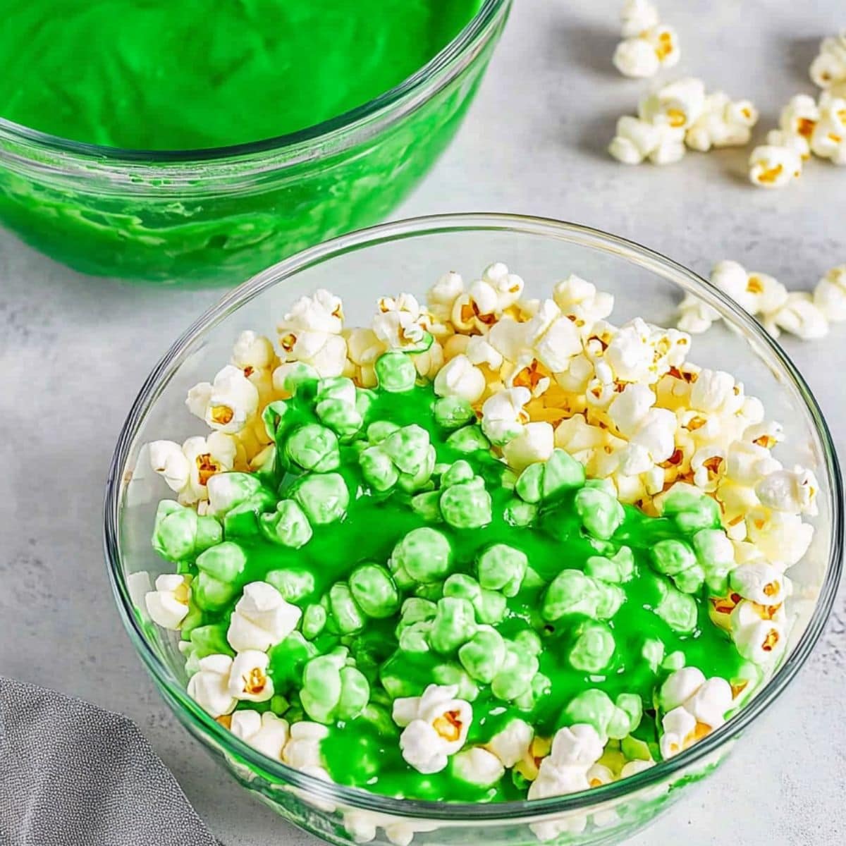 Popcorn in a large glass bowl with green colored melted marshmallows poured over the top