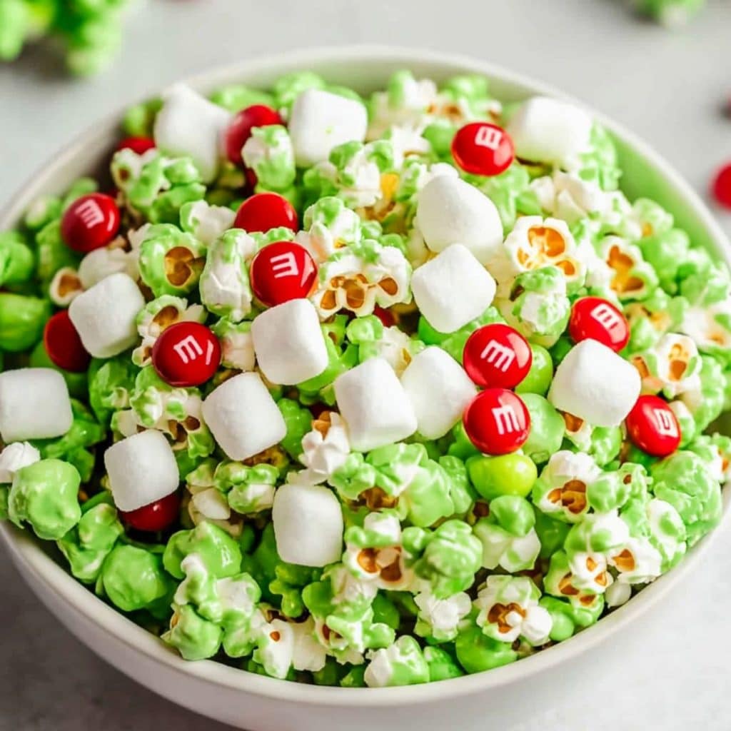 Grinch inspired popcorn with red M&Ms and mini marshmallow served in a white bowl.