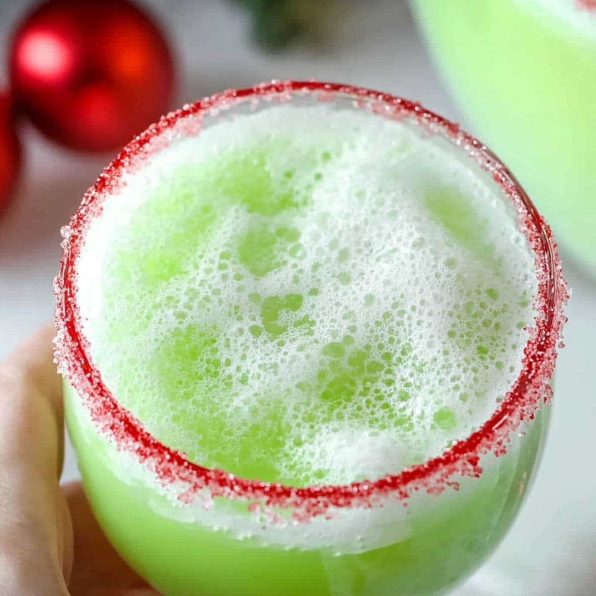 Hand holding Grinch punch served in a red sugar rimmed glass.