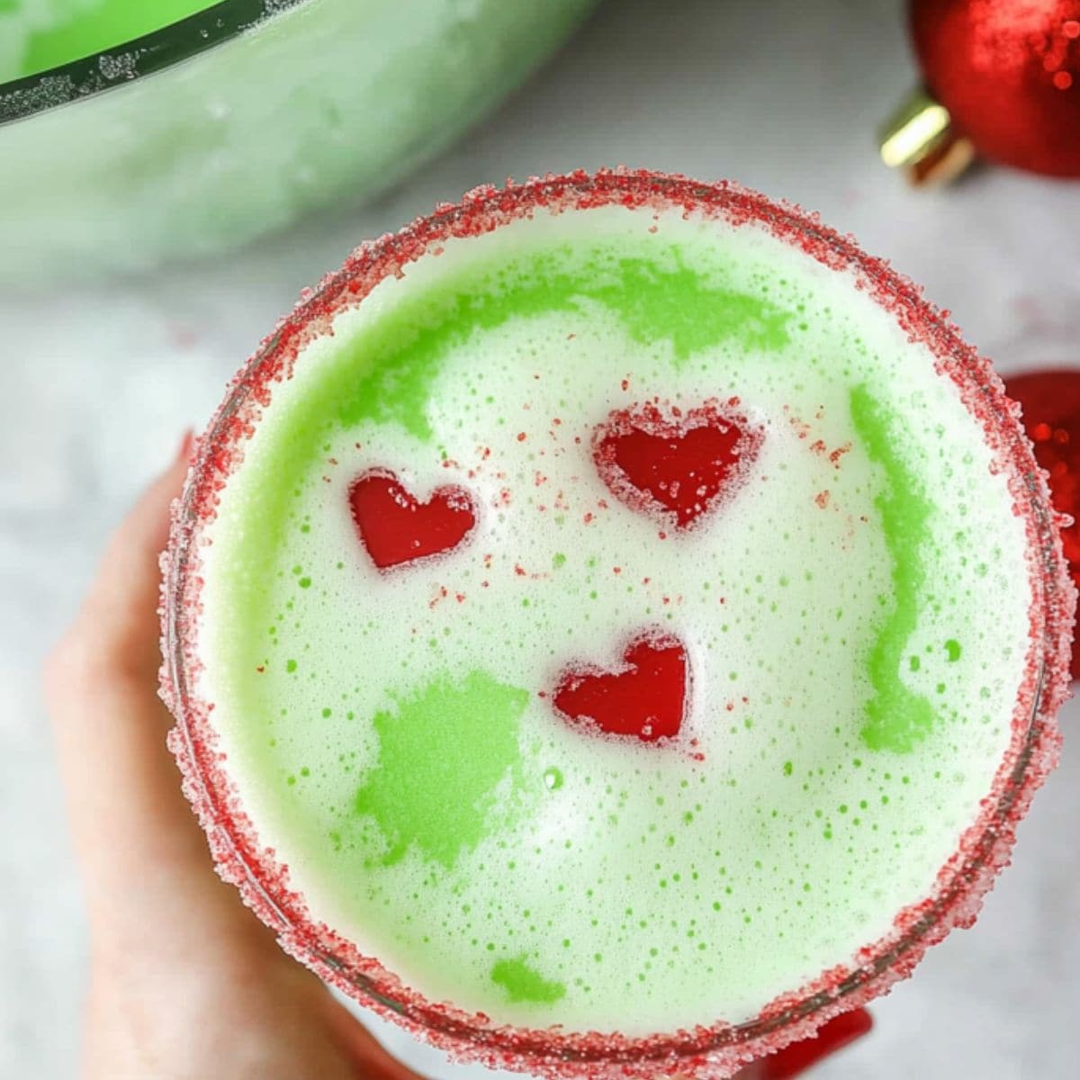 Top view of a Grinch punch served in a sugar rimmed glass with heart shaped sprinkles. 