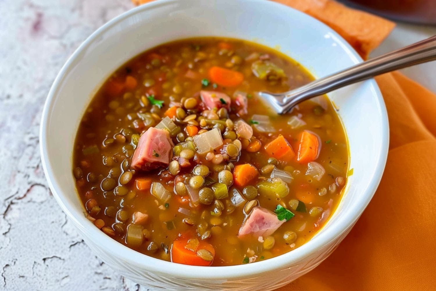 Soup with lentils, chopped ham, bacon and celery served in a white bowl.