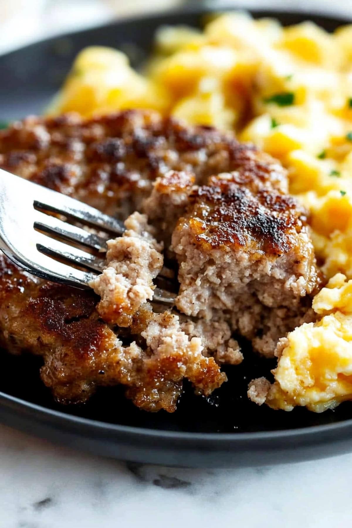 A close-up of a fork slicing a breakfast sausage patty with scrambled eggs.