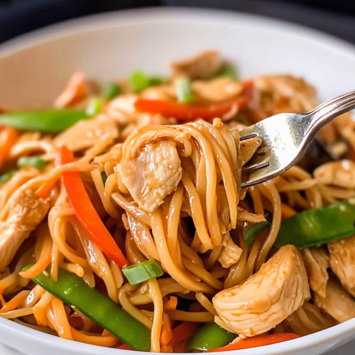 A fork with chicken lo mein and vegetables in a bowl.