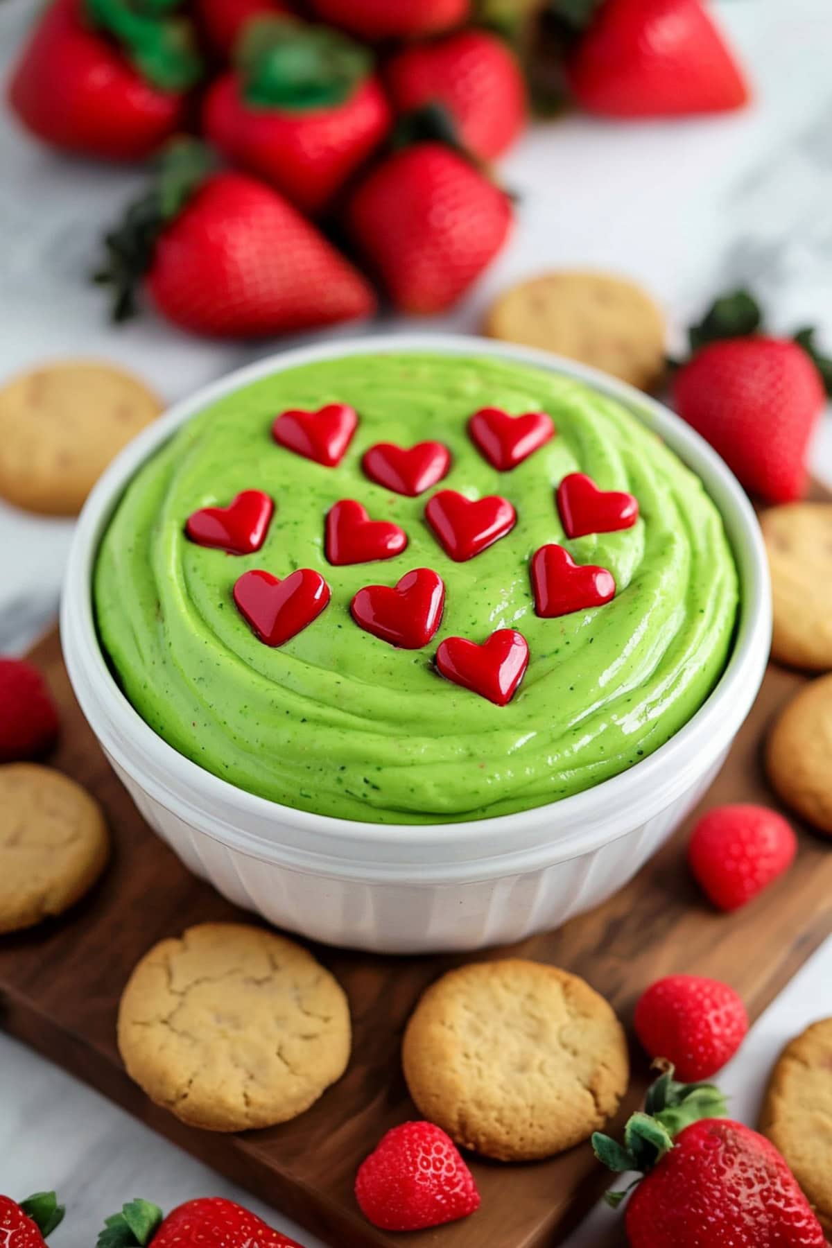 A bowl of homemade grinch dip topped heart-shaped candies.