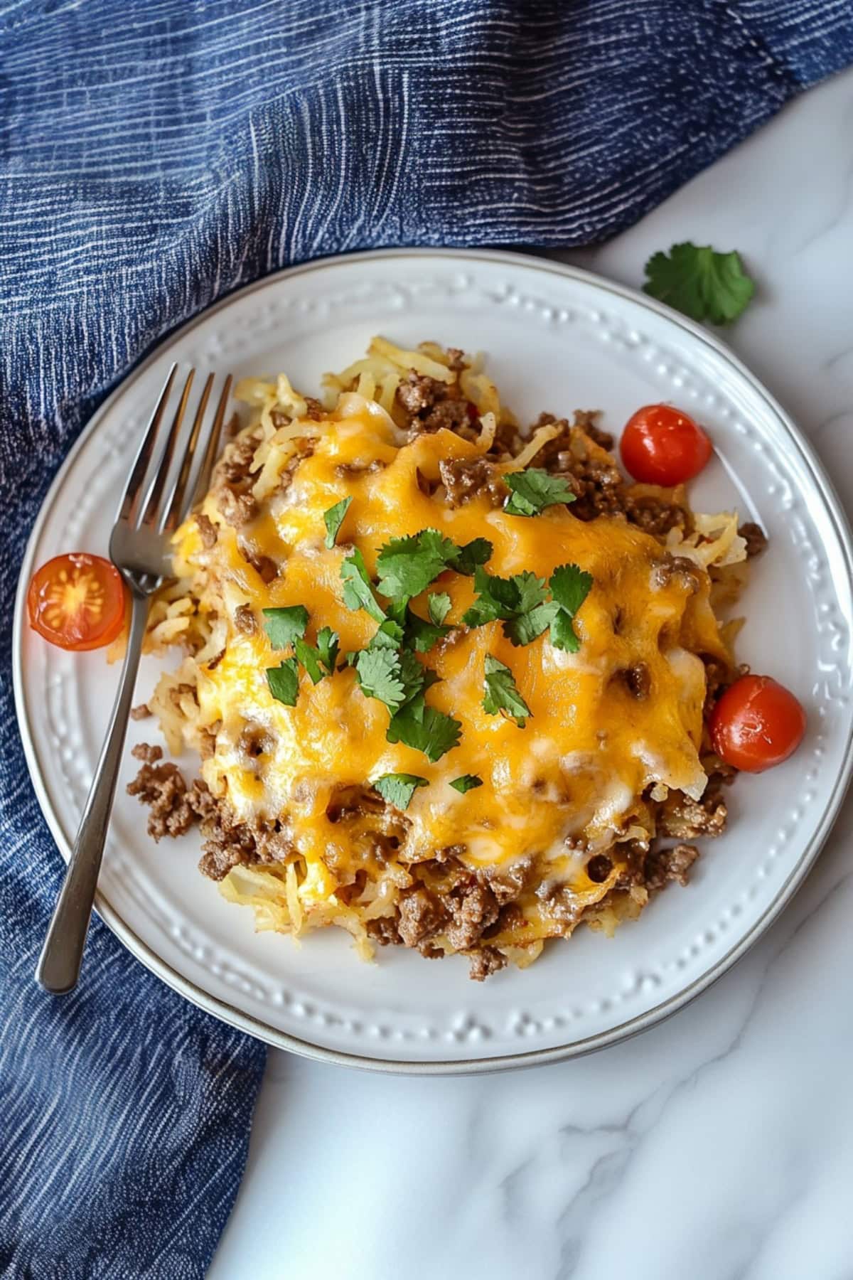 Cheesy taco hashbrown casserole with ground beef, tomatoes and parsley on a plate, top view