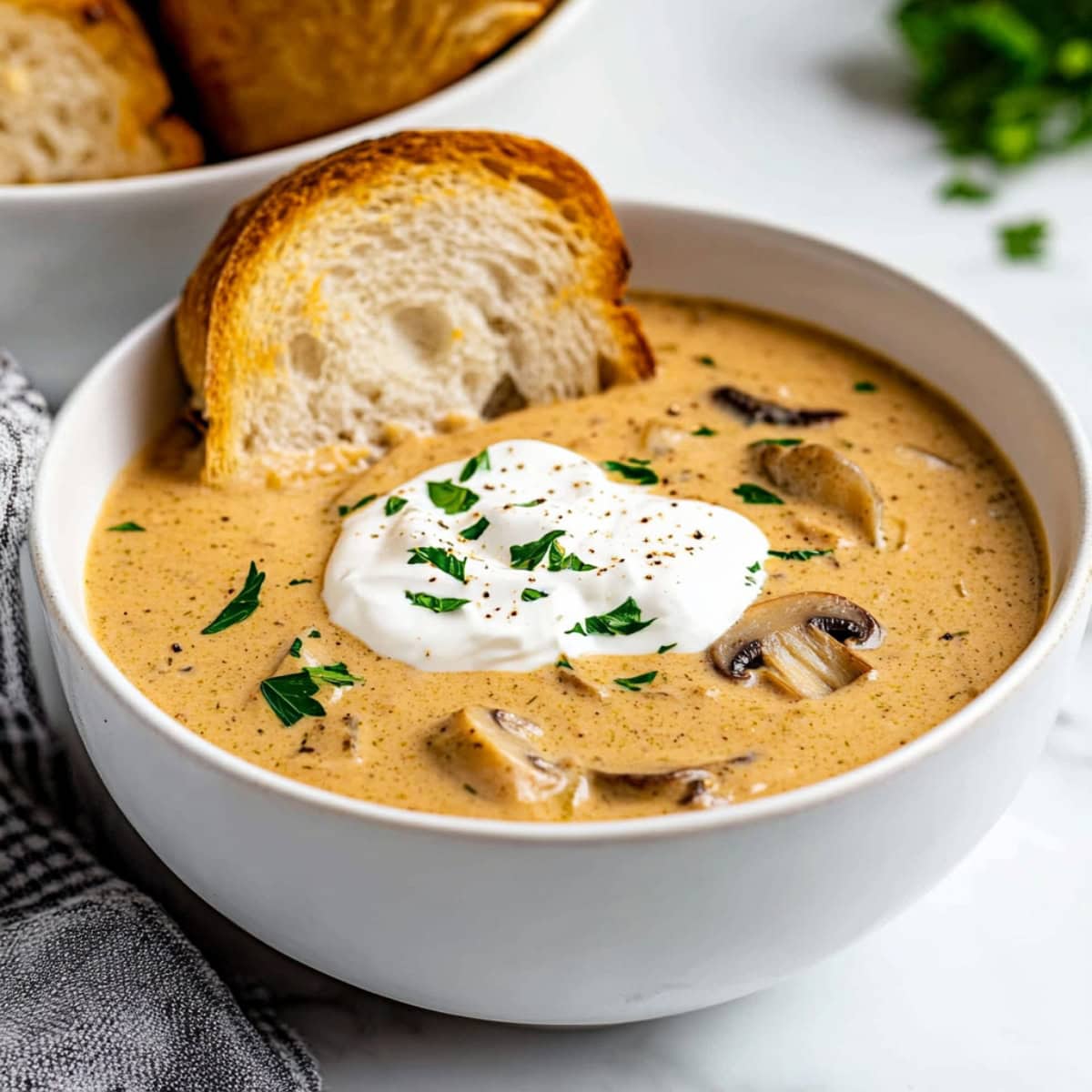 A warm bowl of creamy mushroom soup with sour cream, ground pepper and parsley, served with bread.