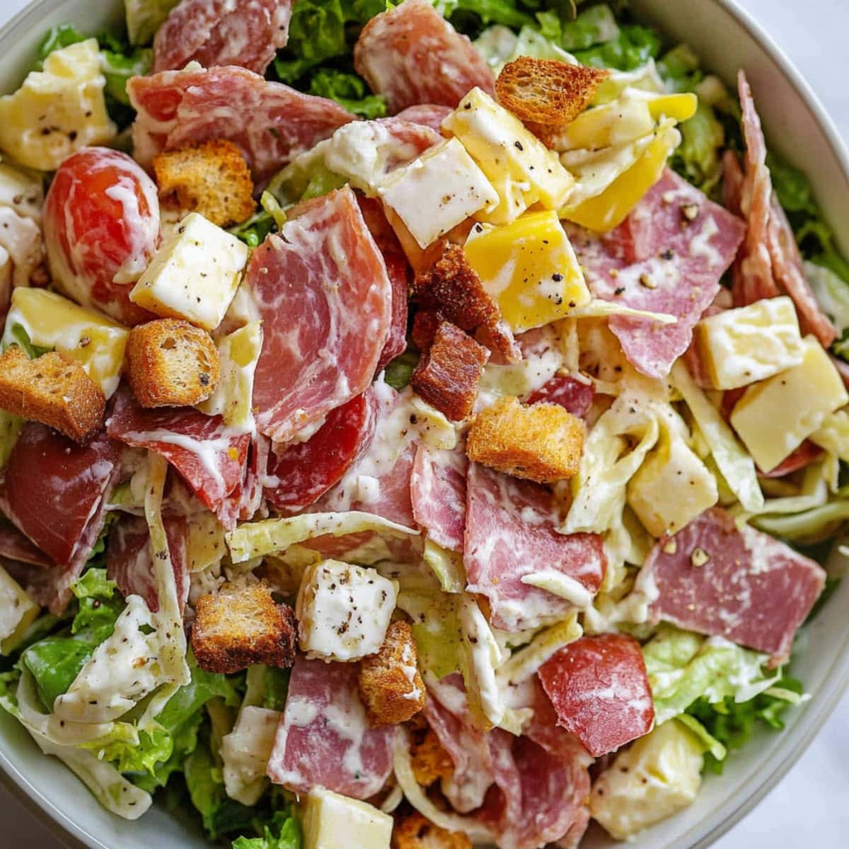 A bowl of creamy Italian grinder salad with tomatoes, croutons, cheese and mets.