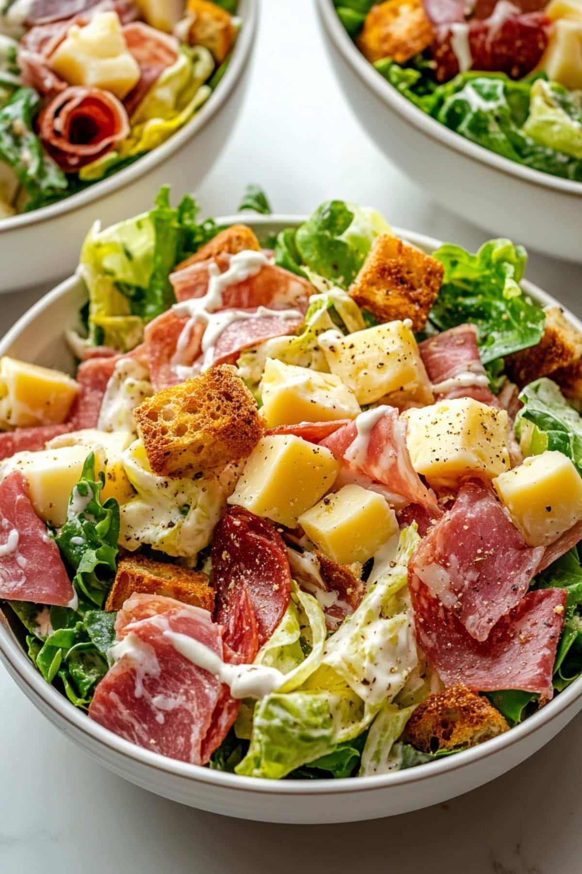 A colorful Italian grinder salad with layers of sliced deli meats, lettuce, cheese and croutons. 