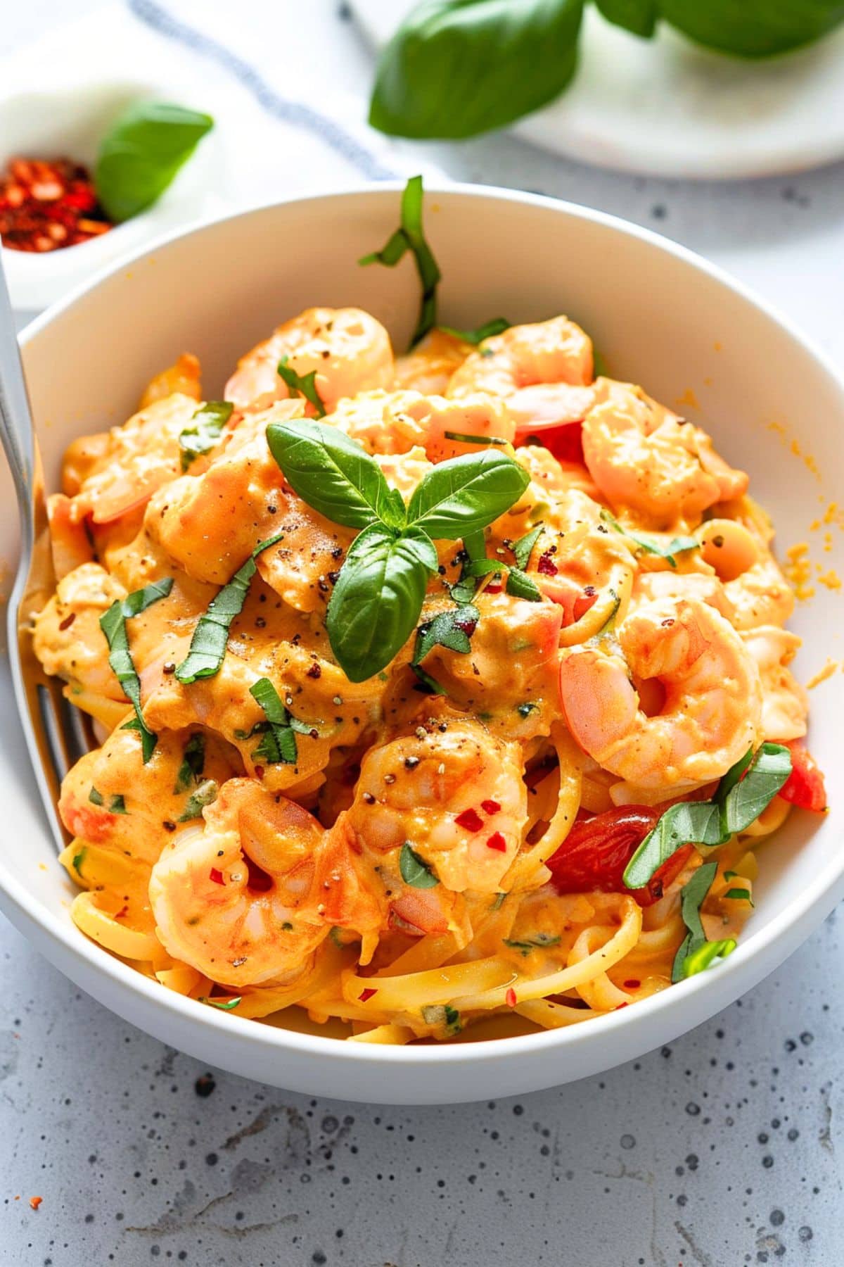 A serving of creamy Marry me shrimp pasta in a bowl with shrimp garnished with fresh basil leaf.