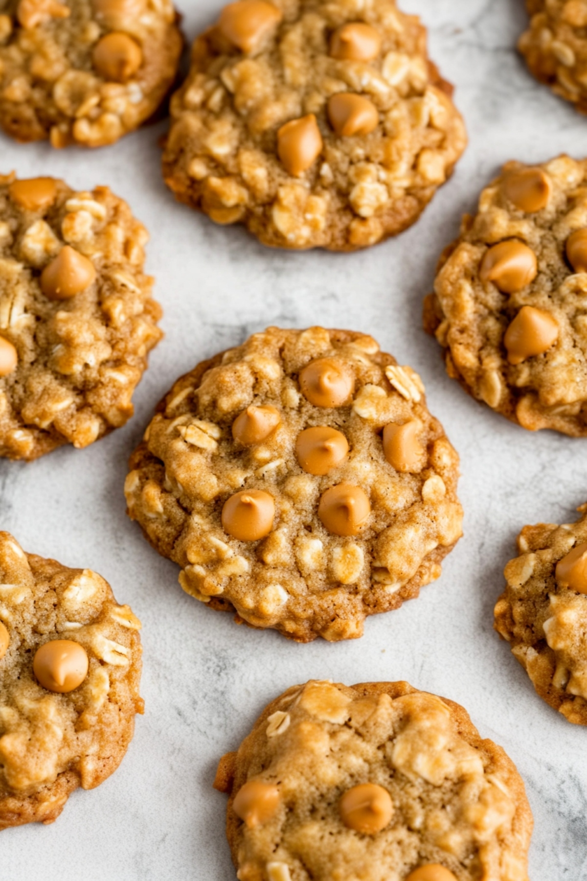 A batch of oatmeal scotchies with golden butterscotch chips, freshly baked on a white marble table.